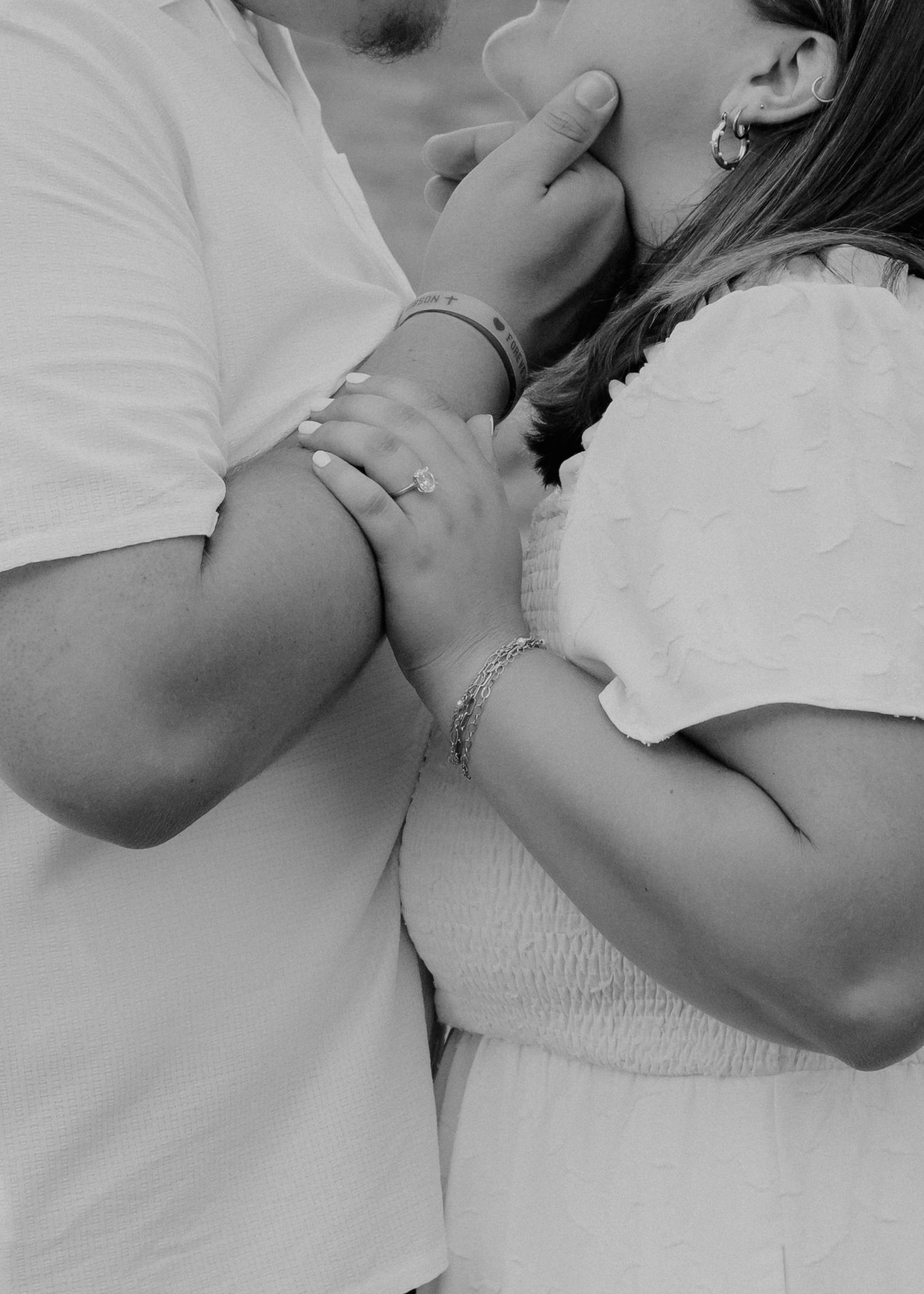 Black and white photo of a couple holding hands and kissing, woman wearing an engagement ring and bracelet.