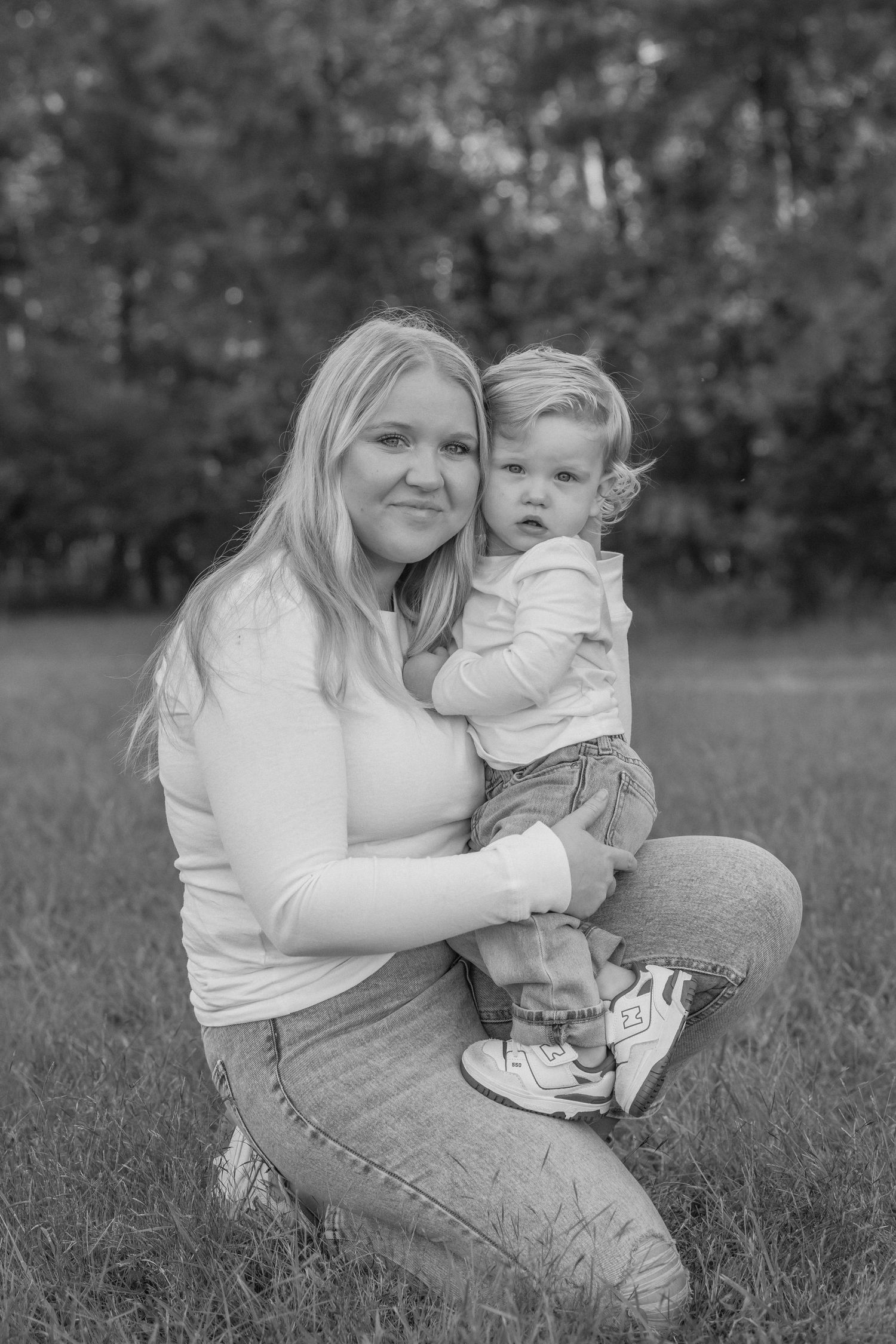 A tender black and white photo series showing a parent and small child embracing on grassy ground outdoors.