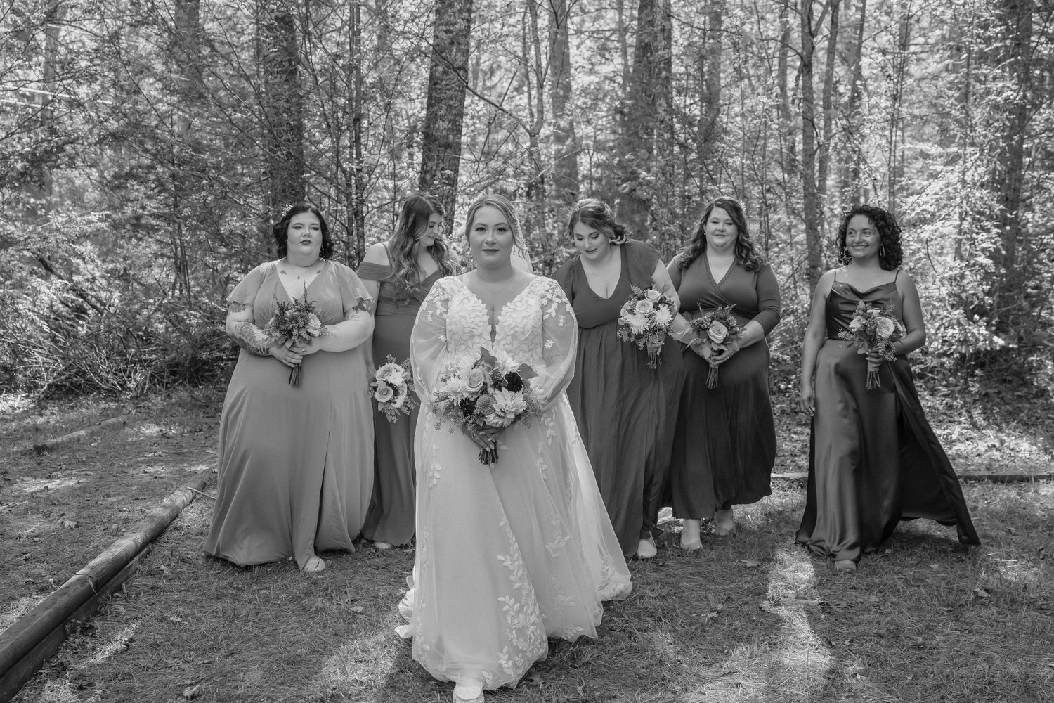 A wedding party poses together in a wooded area wearing coordinated formal attire in shades of blue and gray.