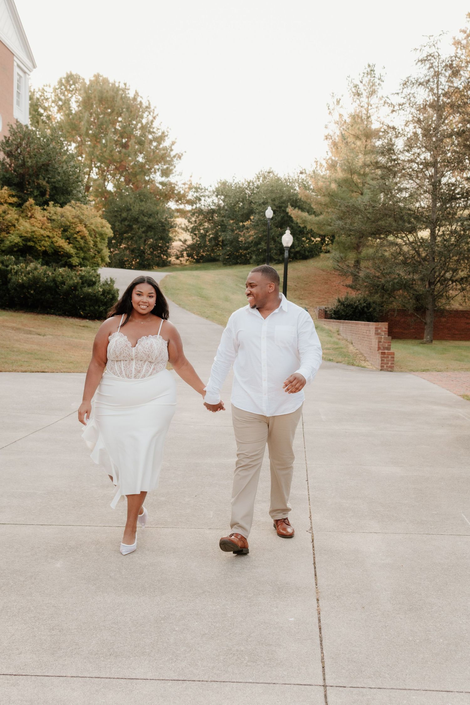 A couple in white outfits dancing and walking together on a concrete path during a sunny day.
