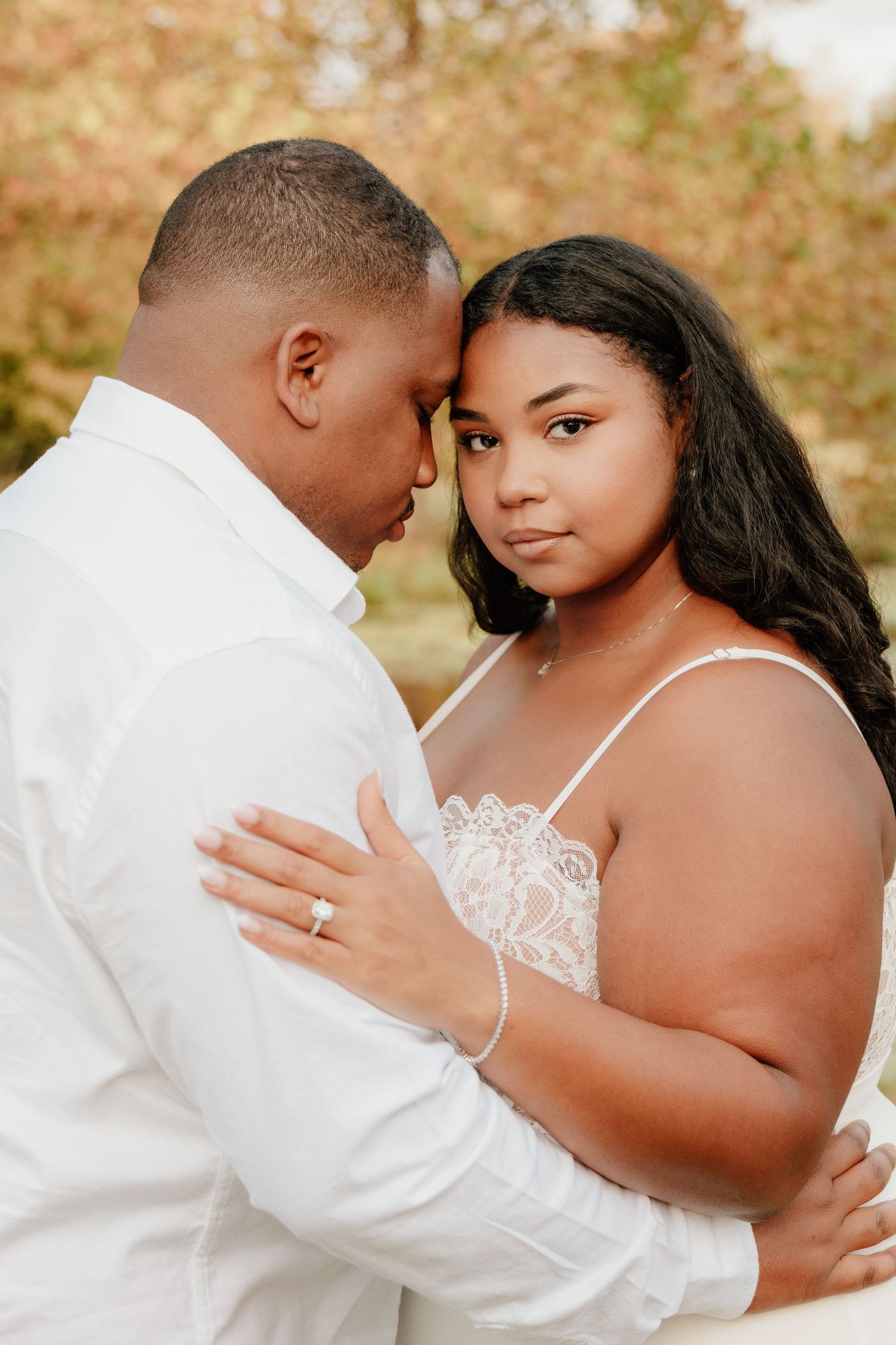 A romantic couple in white attire shares intimate moments during an outdoor autumn photoshoot.