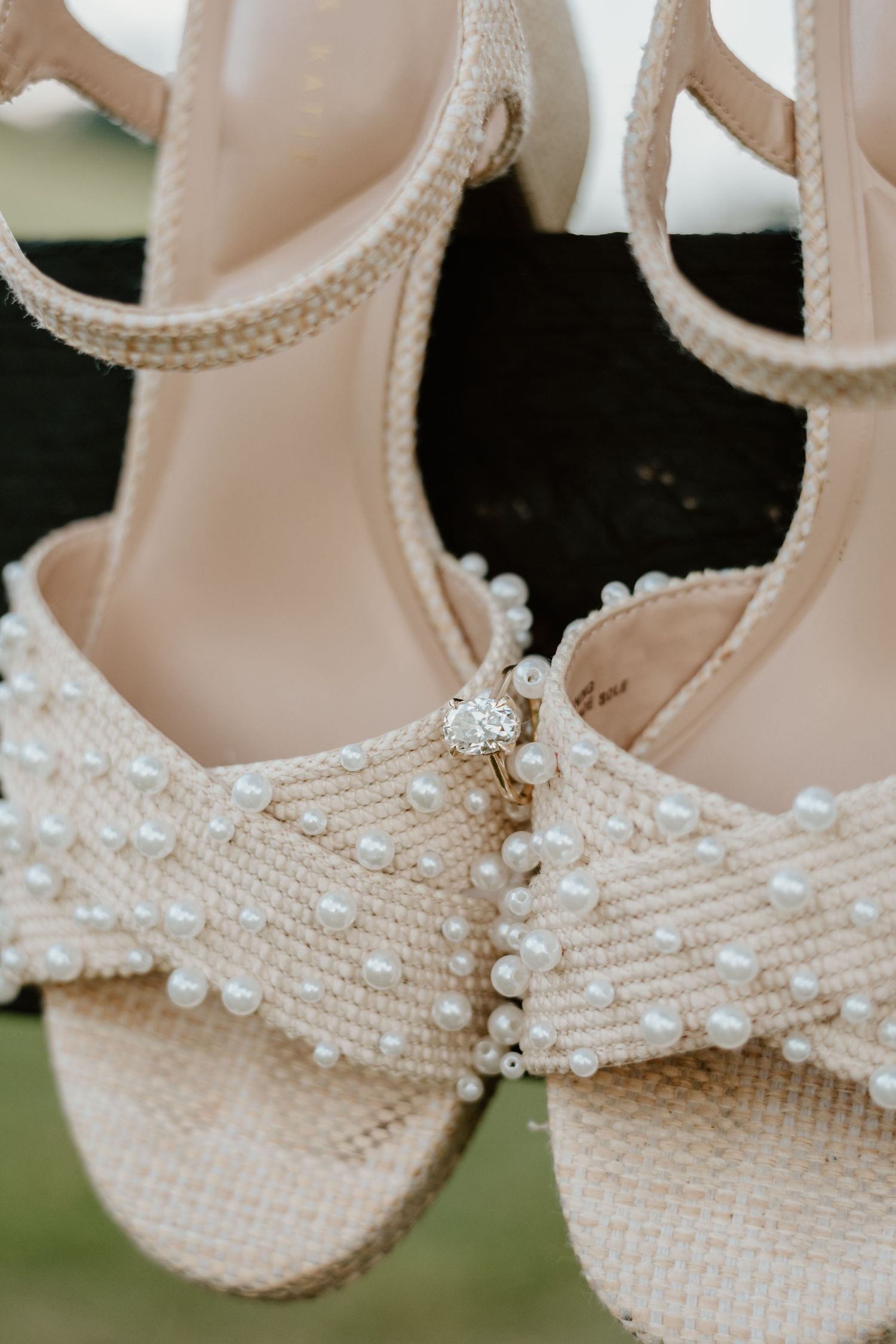 Pearl-embellished bridal heeled sandals with ankle strap and diamond engagement ring resting on toe strap.