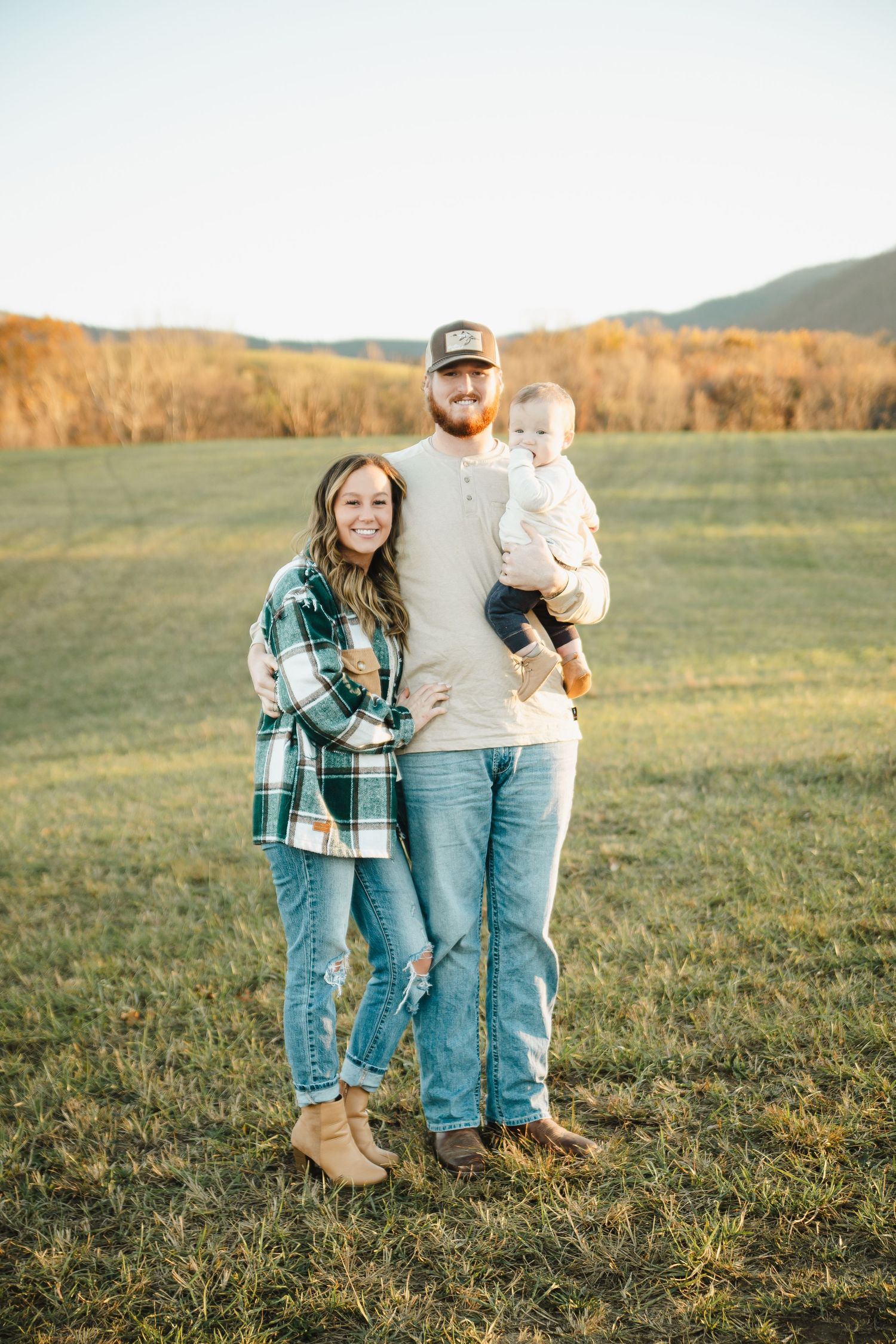 A family poses together in a grassy field at sunset with mountains in the background.
