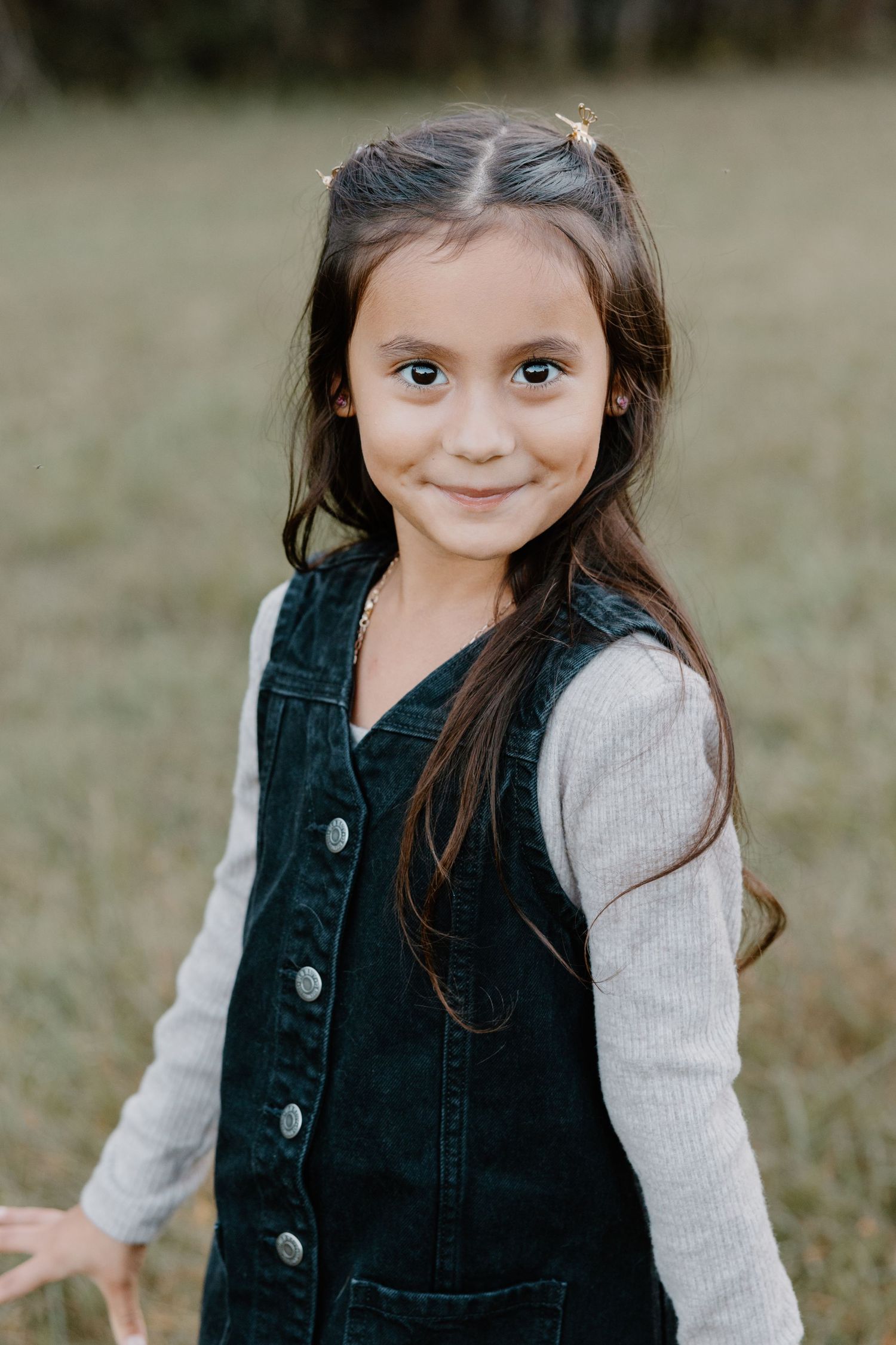 A young child in a black vest and white sweater poses in a grassy field.