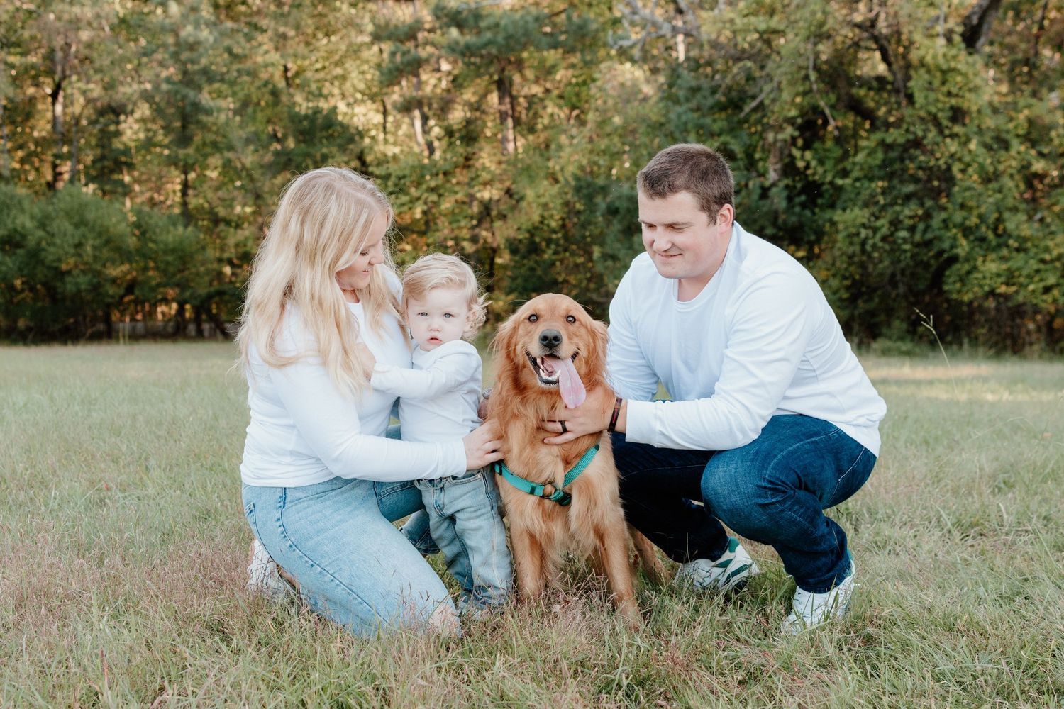 A family and their golden retriever dog sit together on grass during an outdoor photo session.