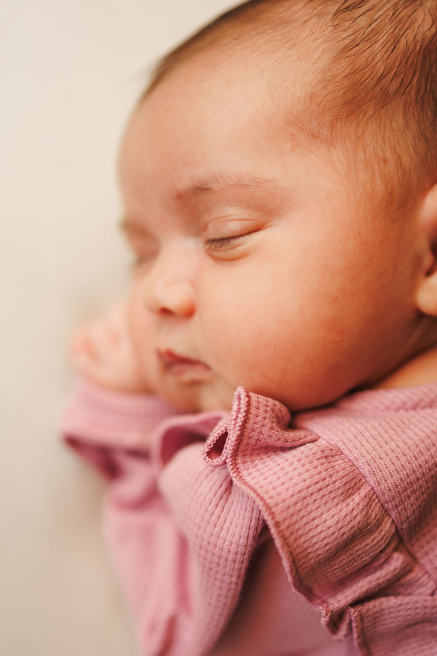 Close-up side view of a sleeping newborn baby wearing a soft pink knitted wrap.