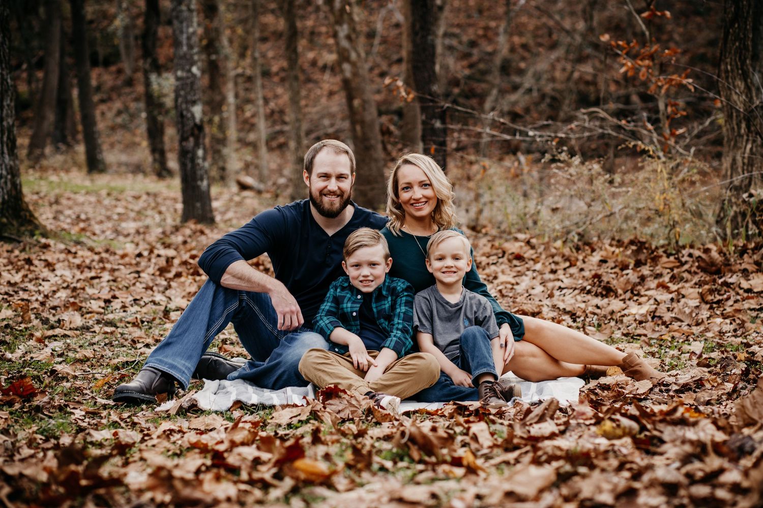 A family group relaxes together on fallen leaves in an autumn forest setting.