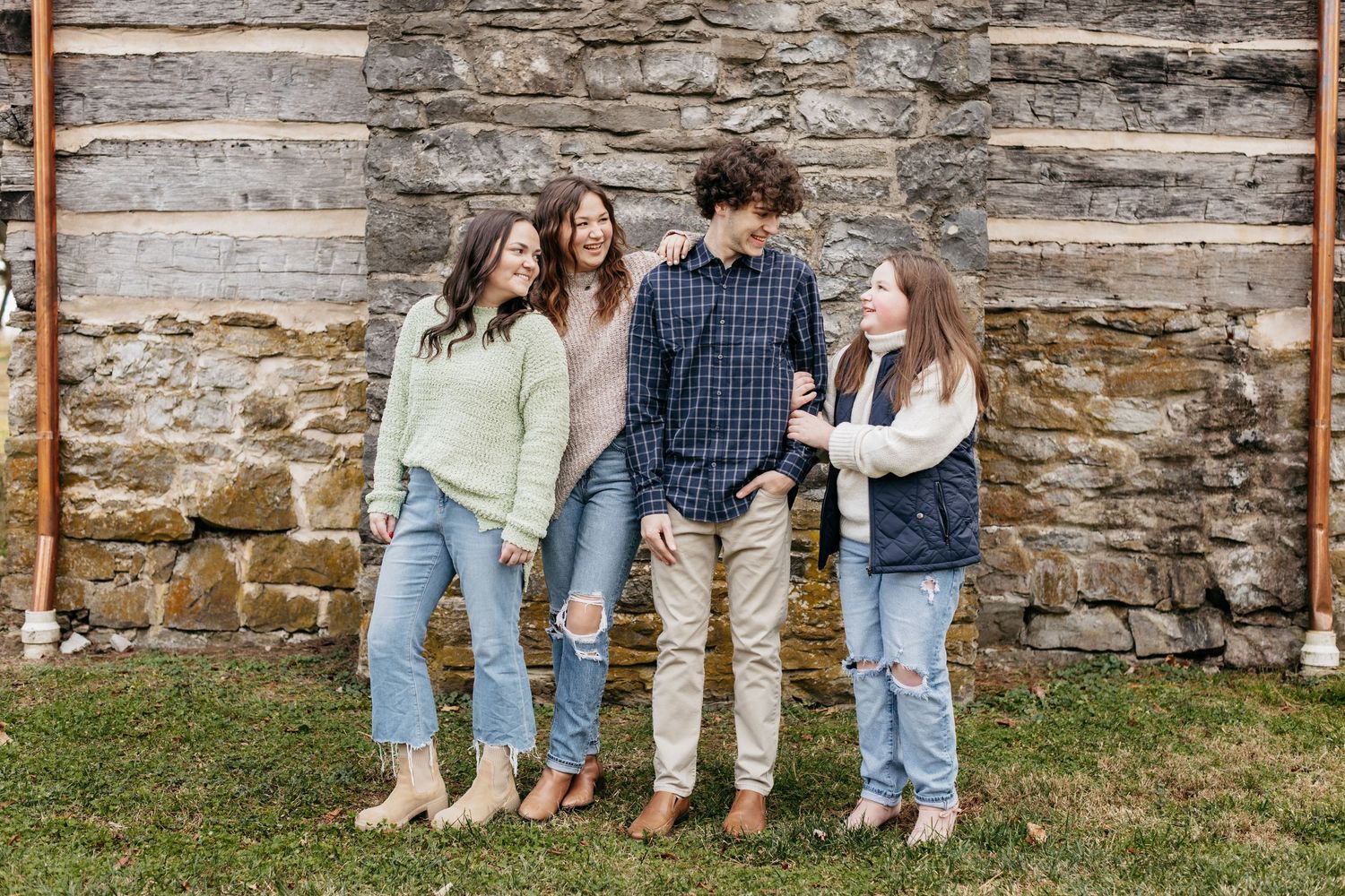 A casual group leans against a weathered stone wall in coordinating casual outfits.