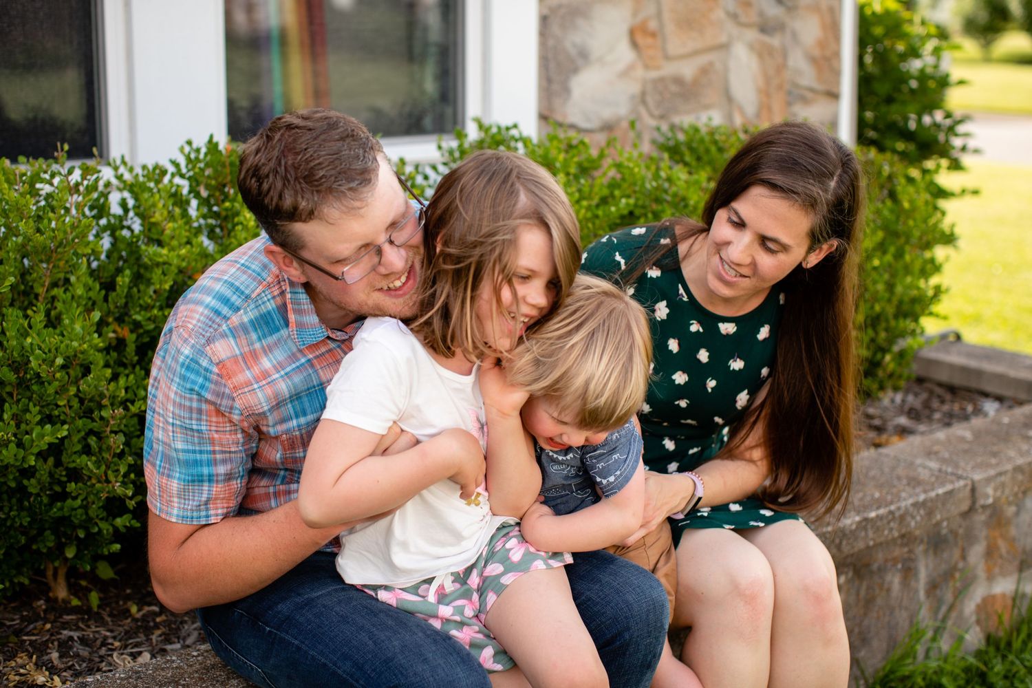 Family sharing a tender moment while sitting together outdoors on a stone wall.