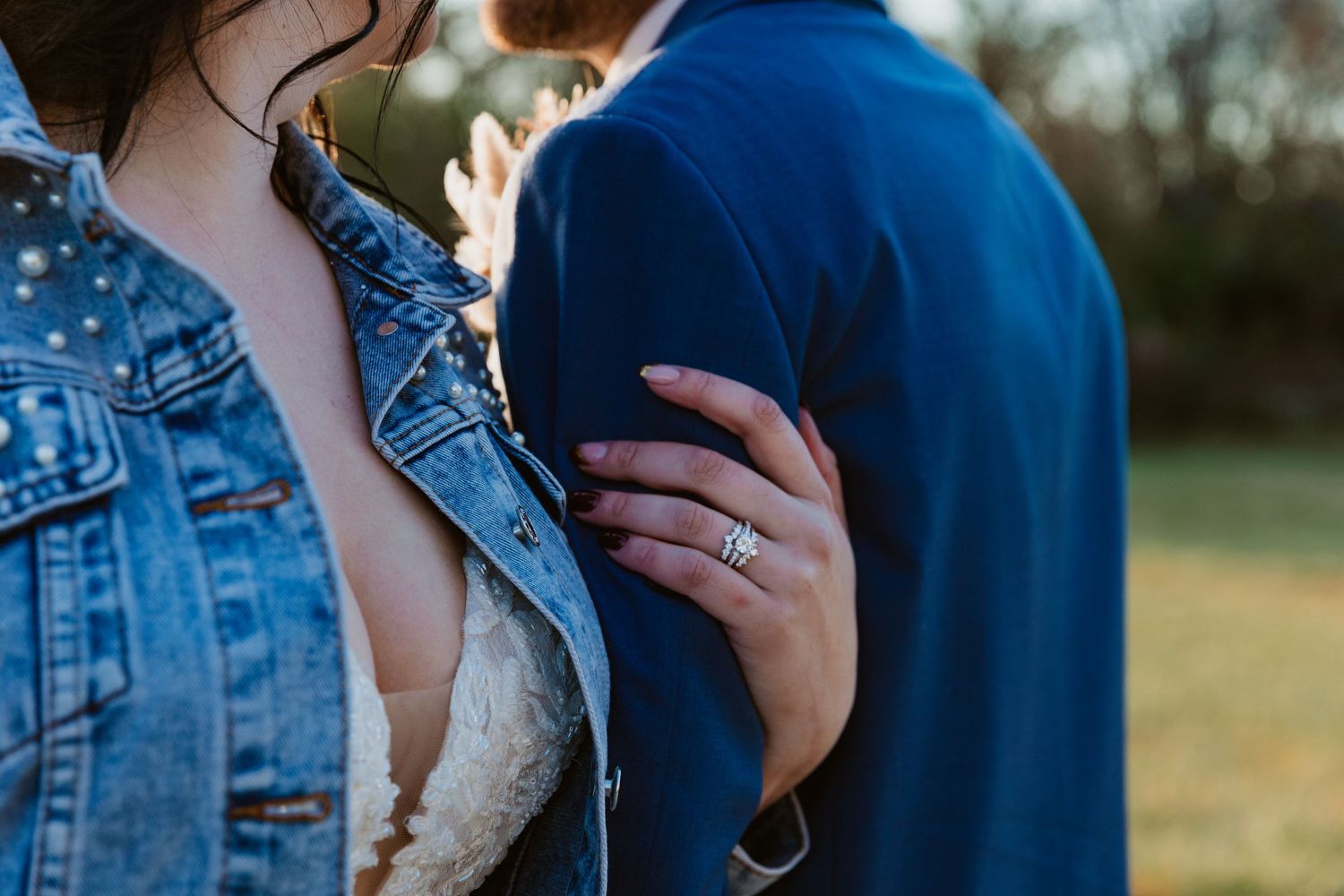 Close-up of an engagement ring as couple embraces outdoors.