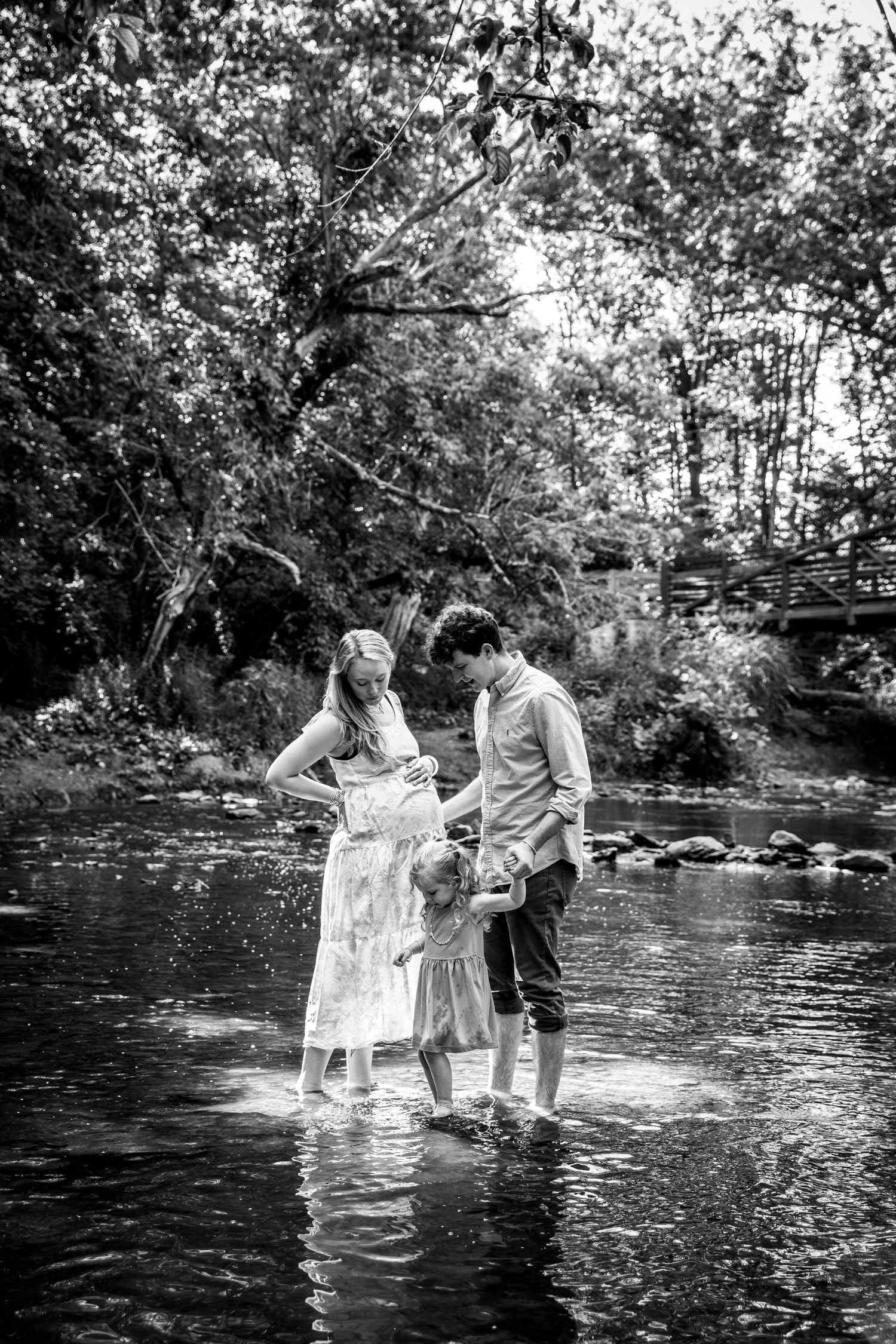 Black and white photo of a family standing in a creek surrounded by trees.