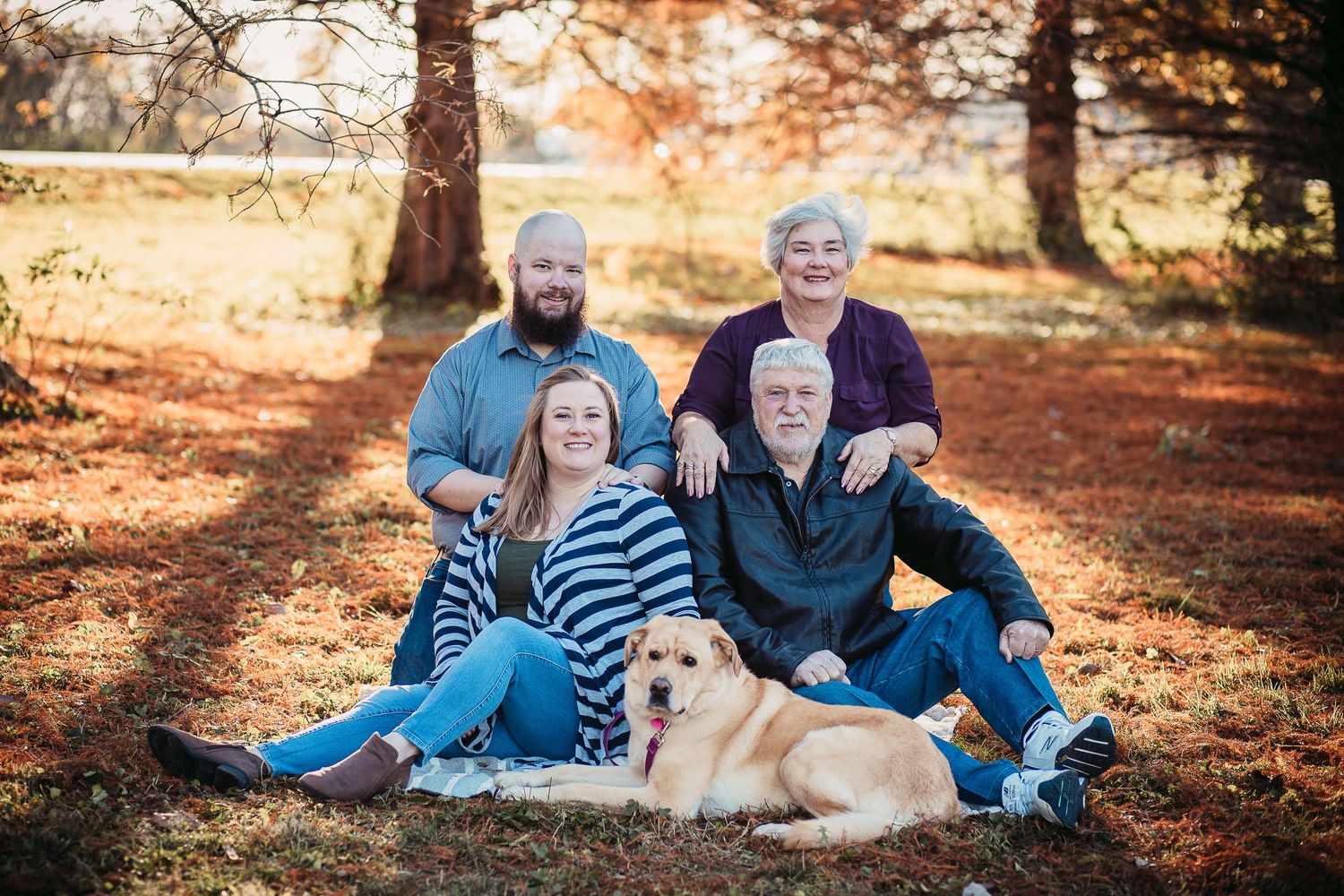 Family and their golden retriever dog posing for a portrait in a fall forest setting.
