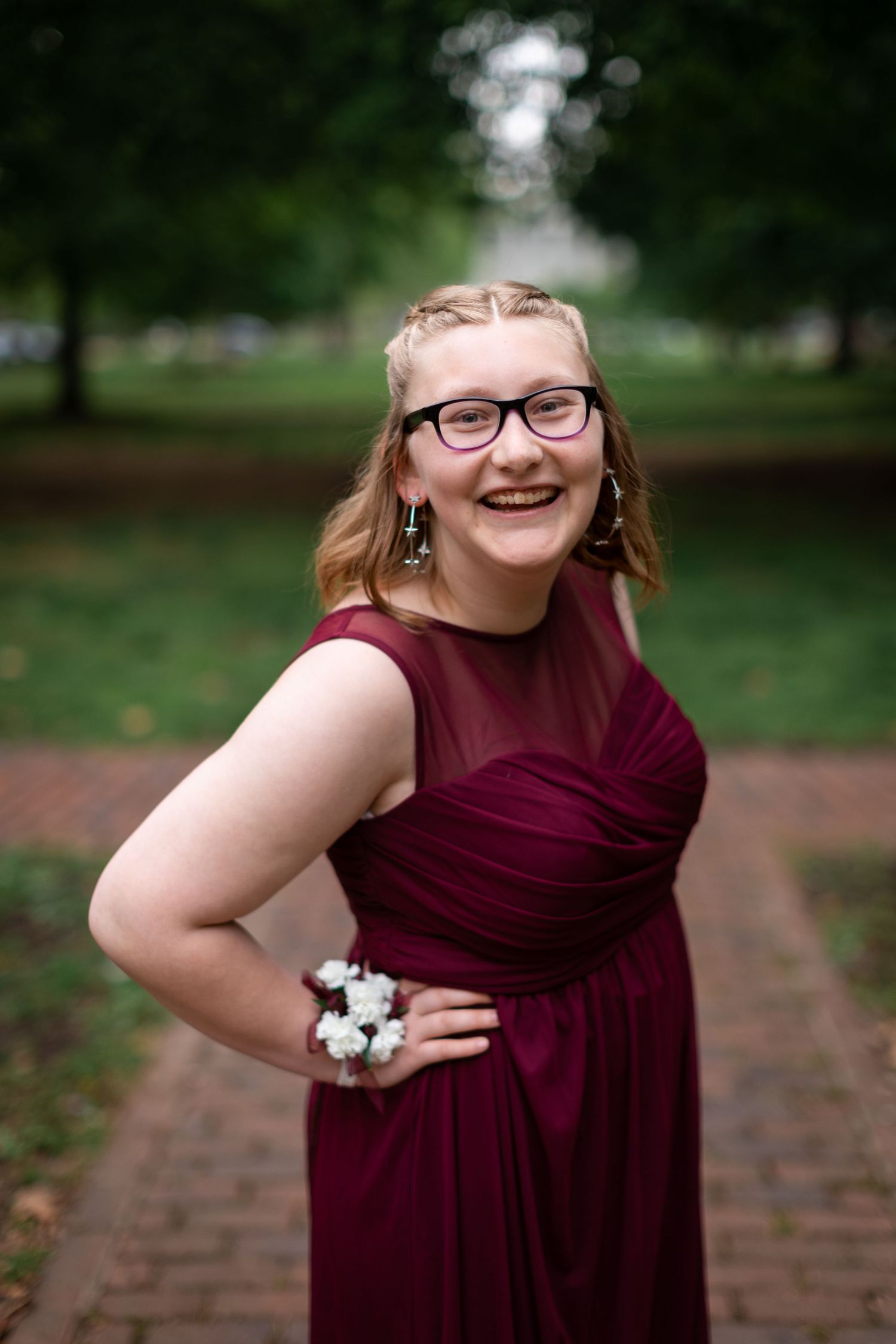 Person in burgundy dress smiles while posing with corsage during formal event photography.