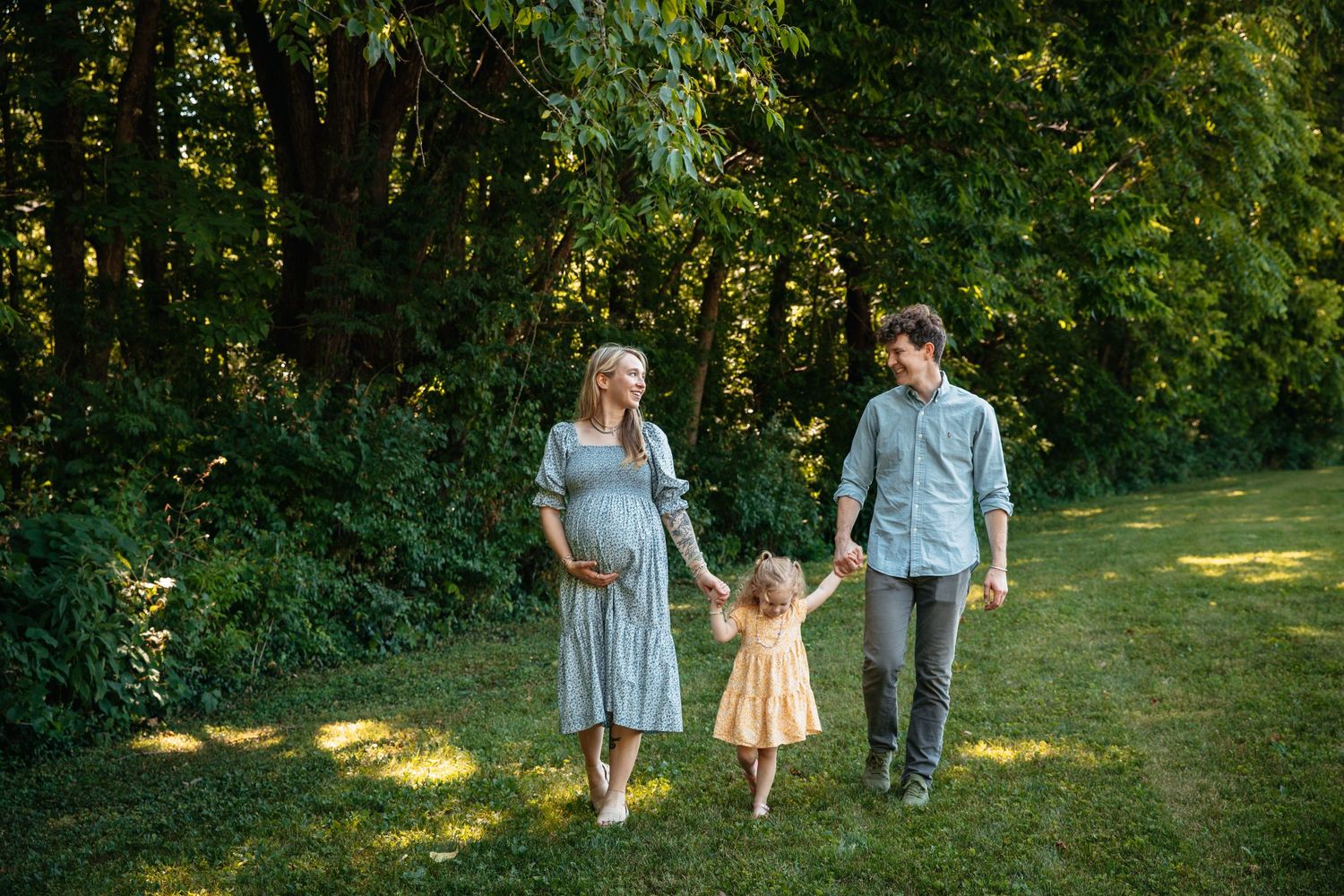 Family holding hands while walking together on a sunny path through greenery.