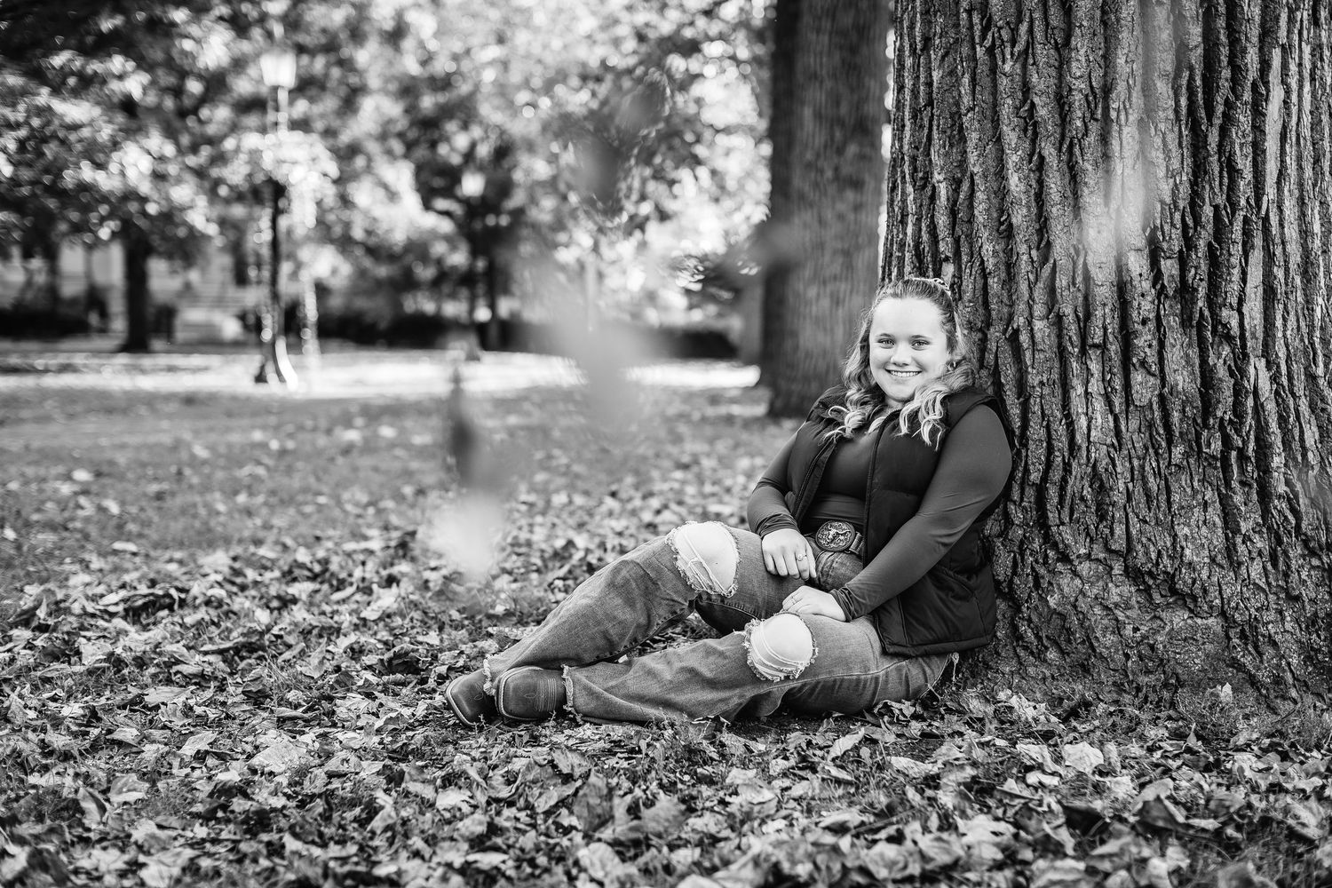A series of black and white photos showing someone resting against a tree trunk surrounded by fallen autumn leaves.