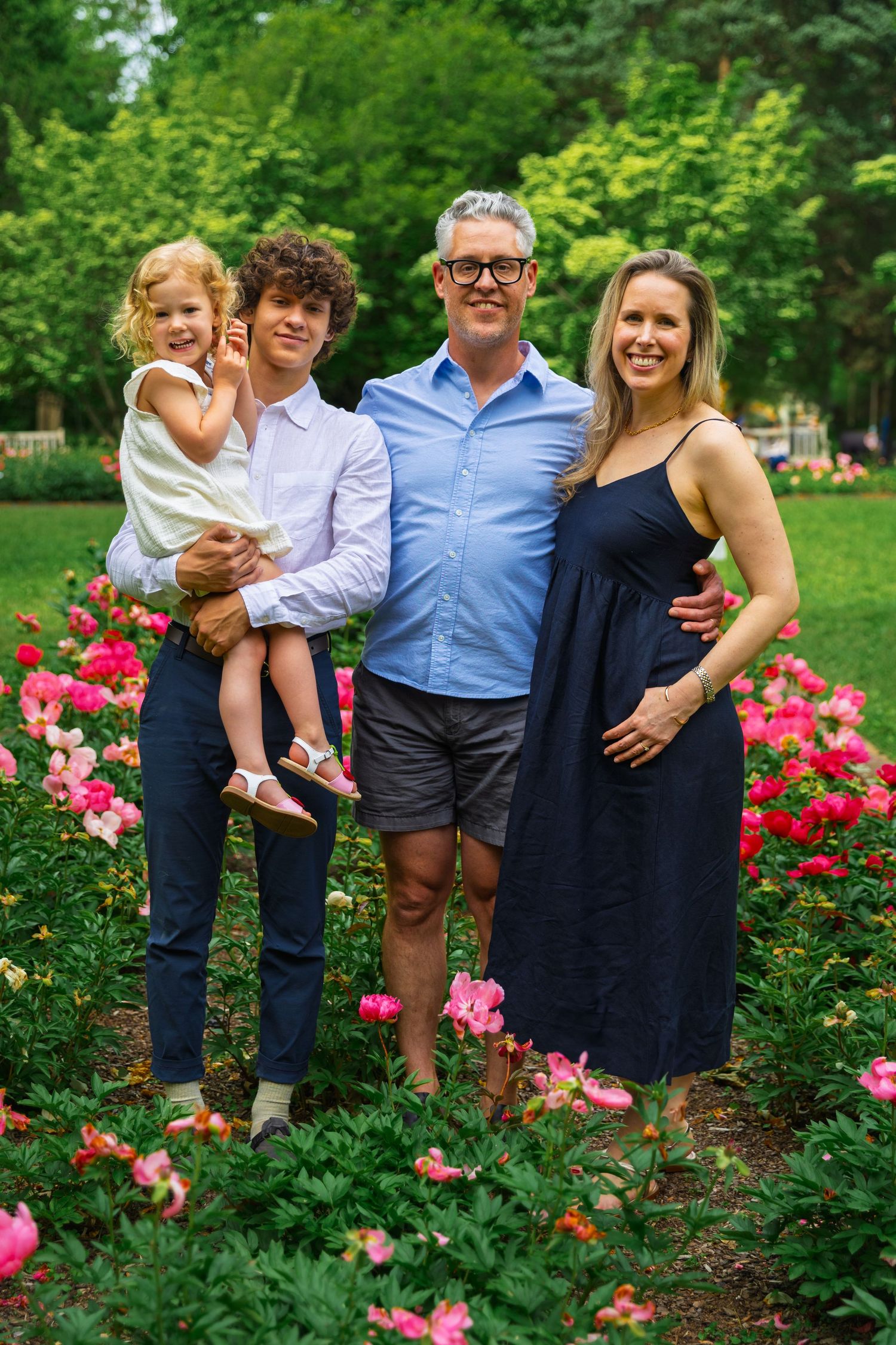 Family portrait surrounded by vibrant pink roses in a garden setting on a sunny summer day.
