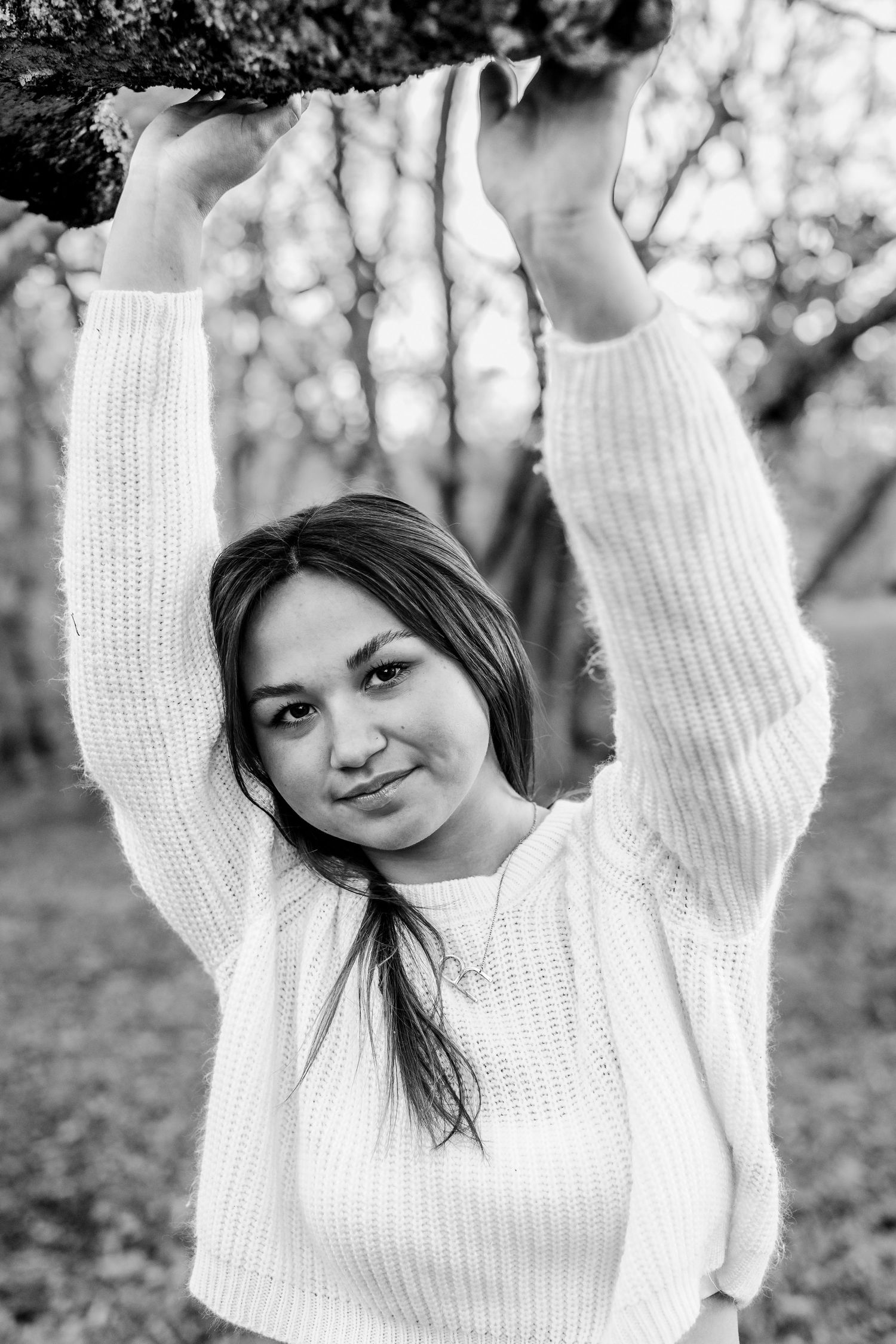 Black and white portrait of someone in a white sweater reaching up with raised arms.