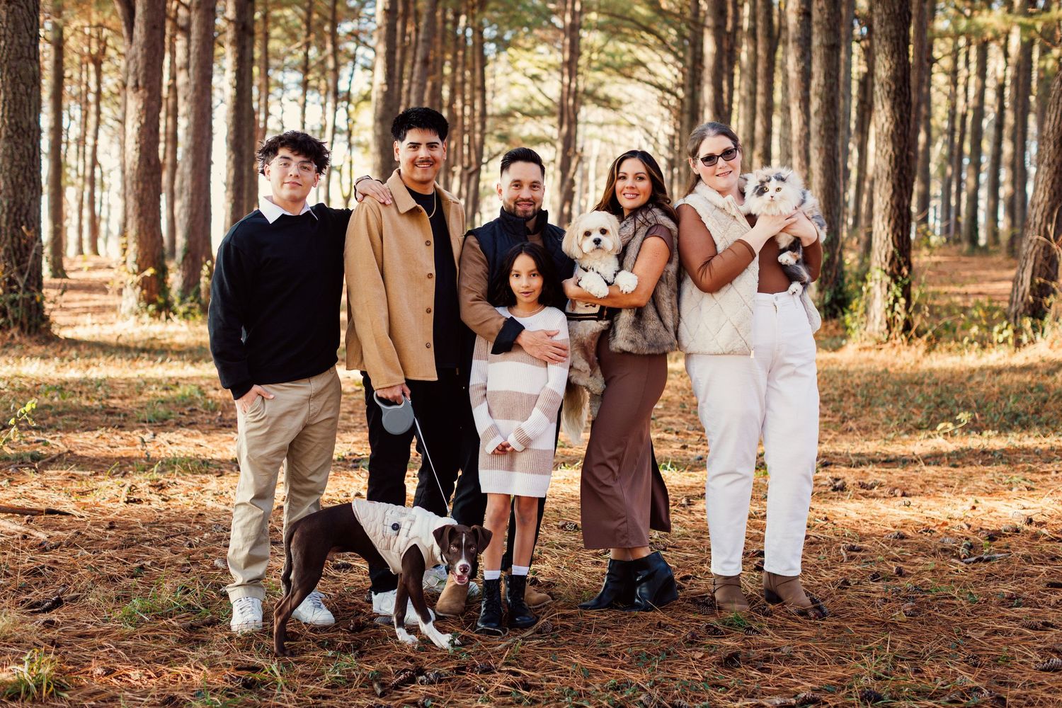 A group poses together for outdoor autumn family photos in a sunlit forest setting.