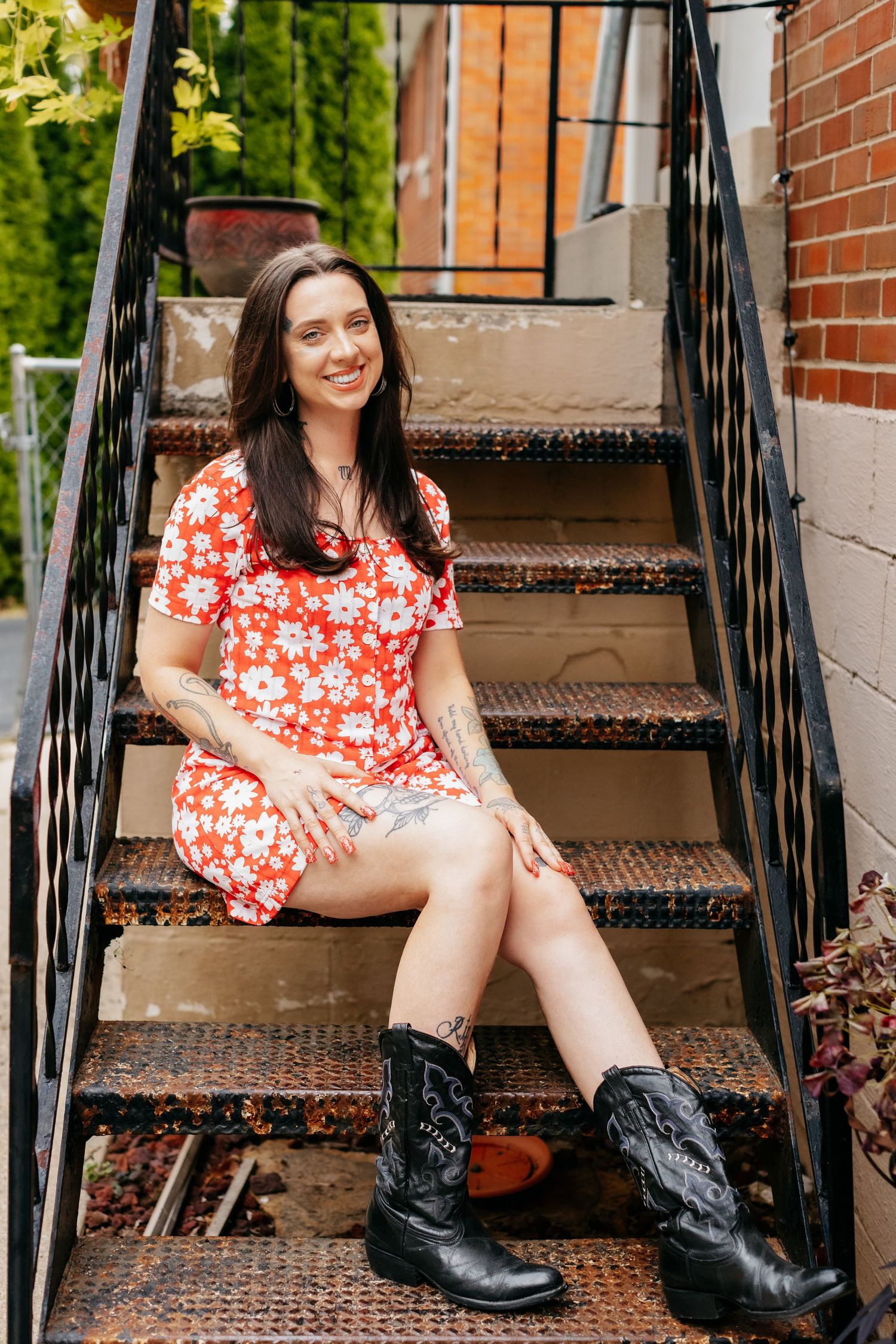 A floral dress and boots outfit on outdoor steps with brick wall backdrop.