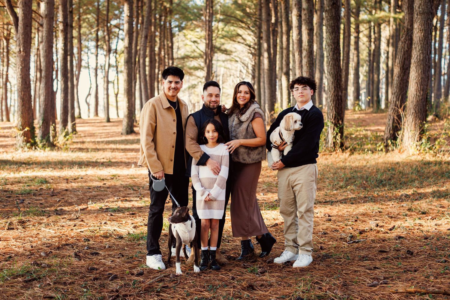 A group stands together with their dog in a scenic pine forest during autumn.