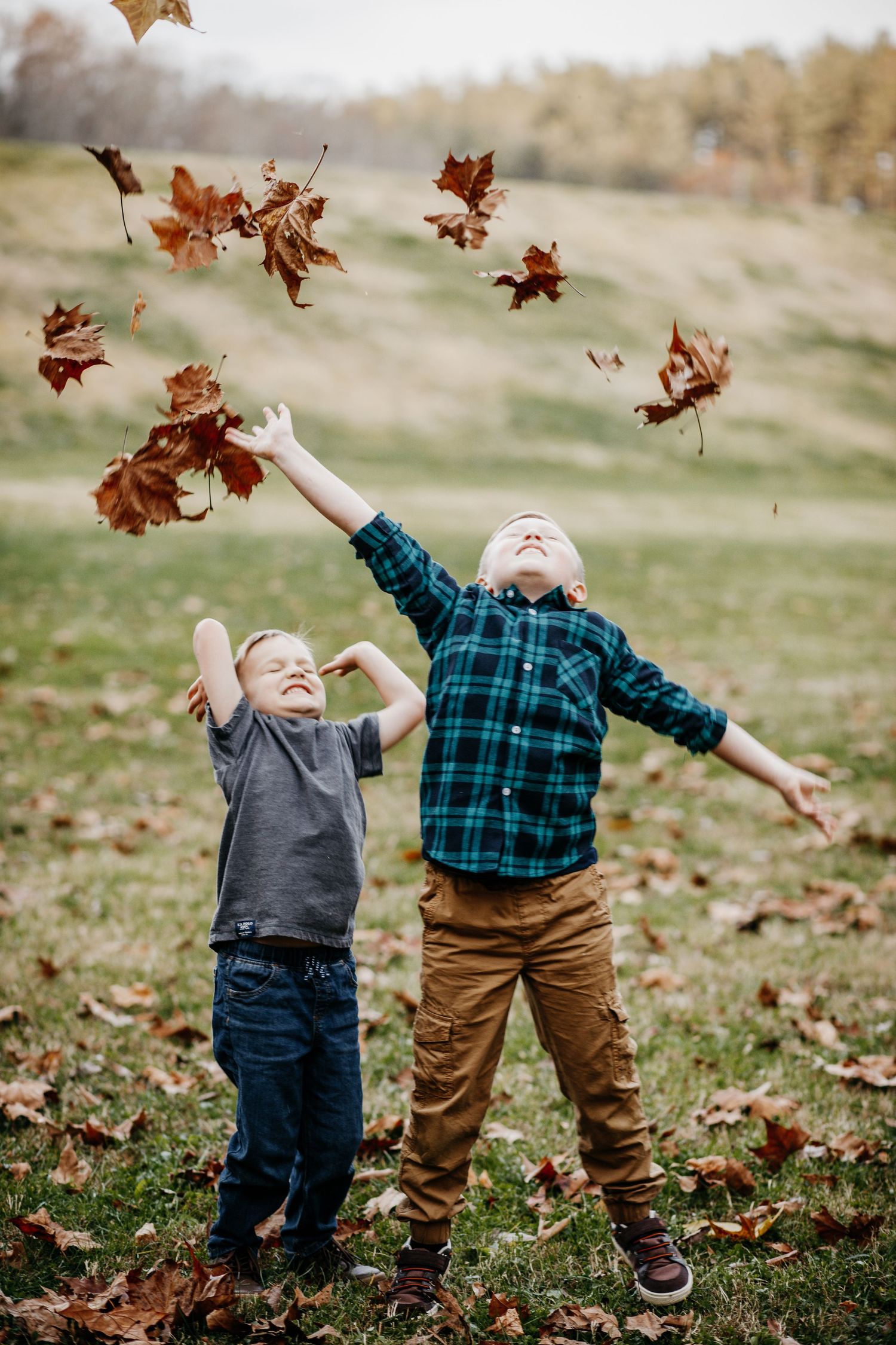 Two children play with falling autumn leaves in a field.
