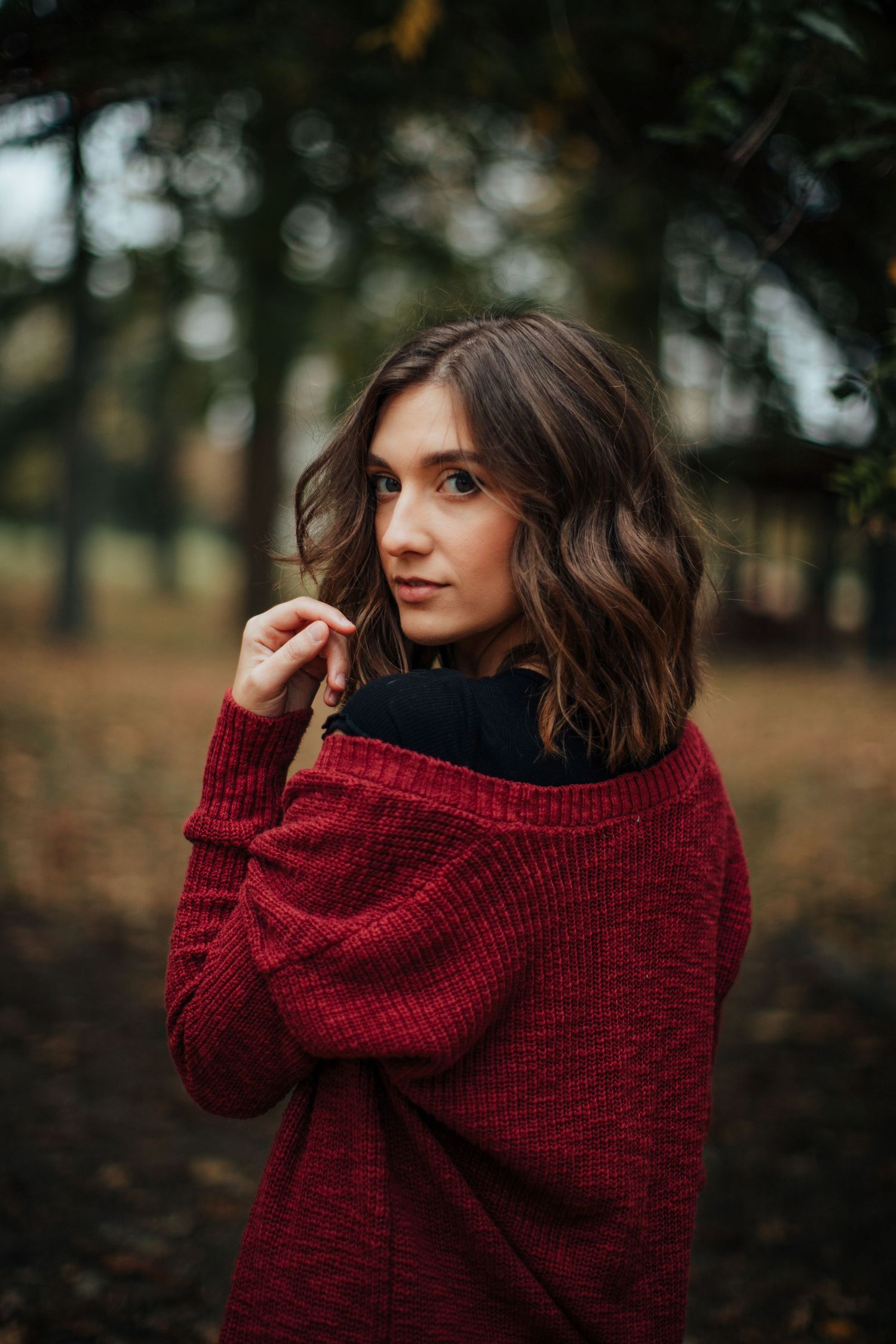 Cozy autumn look with burgundy sweater and turtleneck against blurred forest background.