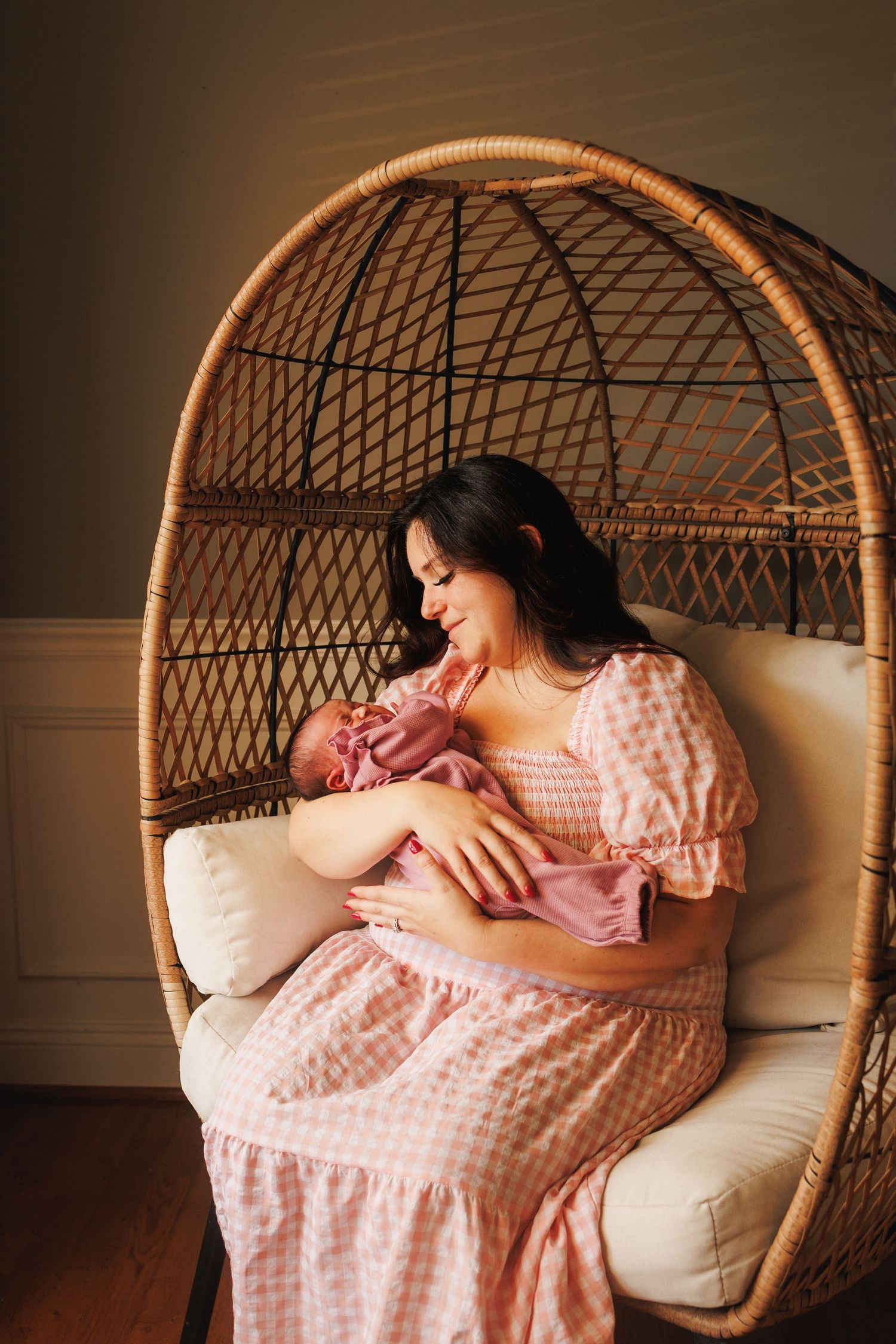 A series of intimate moments captured in a rattan hanging chair showing tender maternal bonding in pink gingham dress.