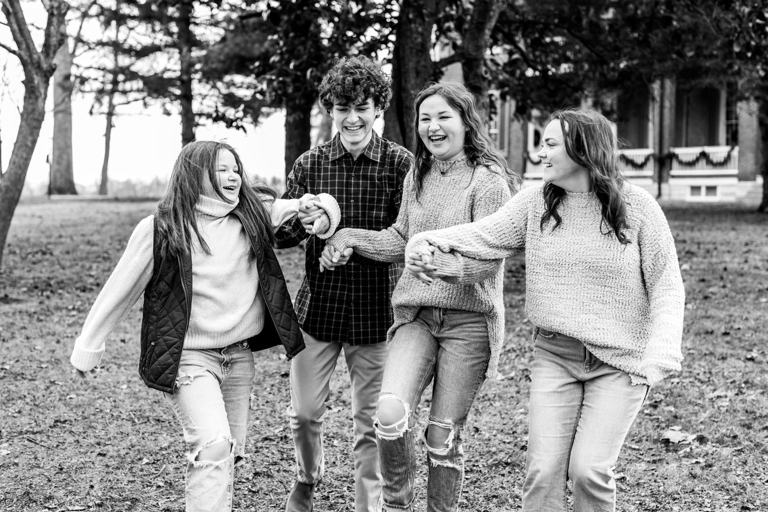 Four cousins laughing and walking together in a park setting captured in black and white.