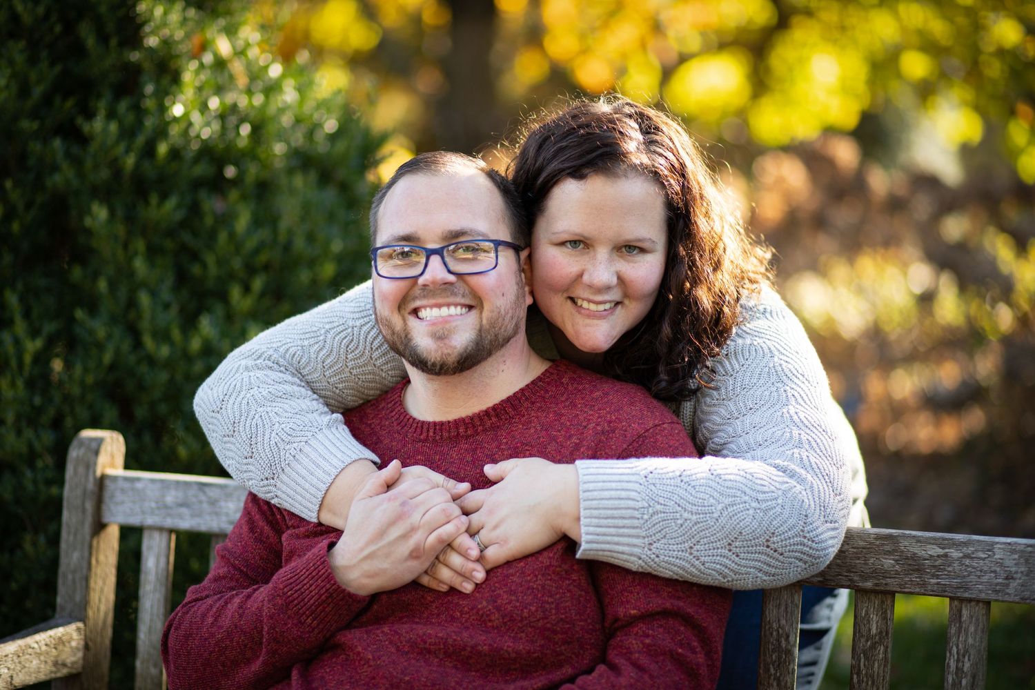 A couple shares a joyful embrace while sitting on a wooden bench in an autumn setting.