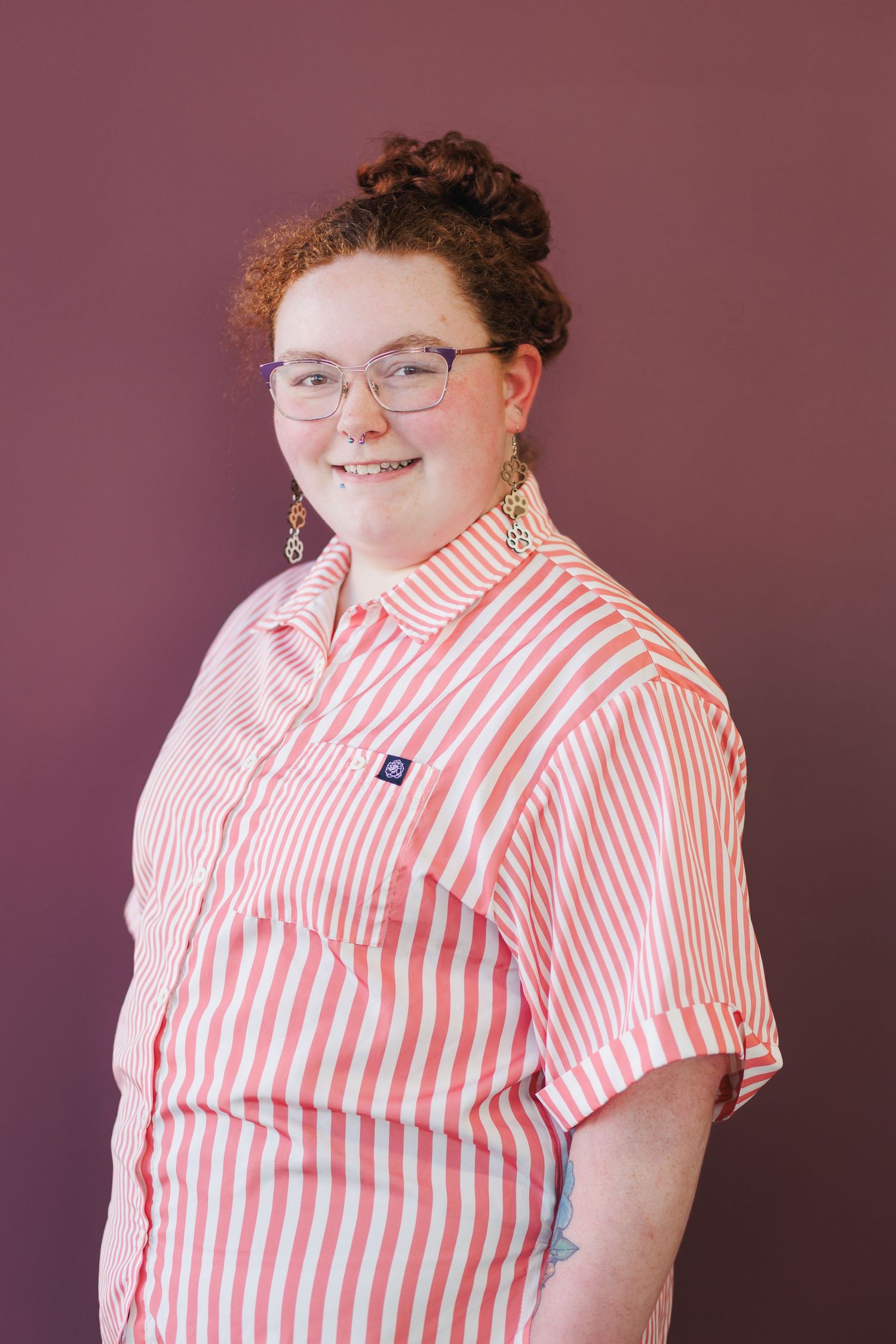 Person wearing a red and white striped collared shirt smiling against a dark background.