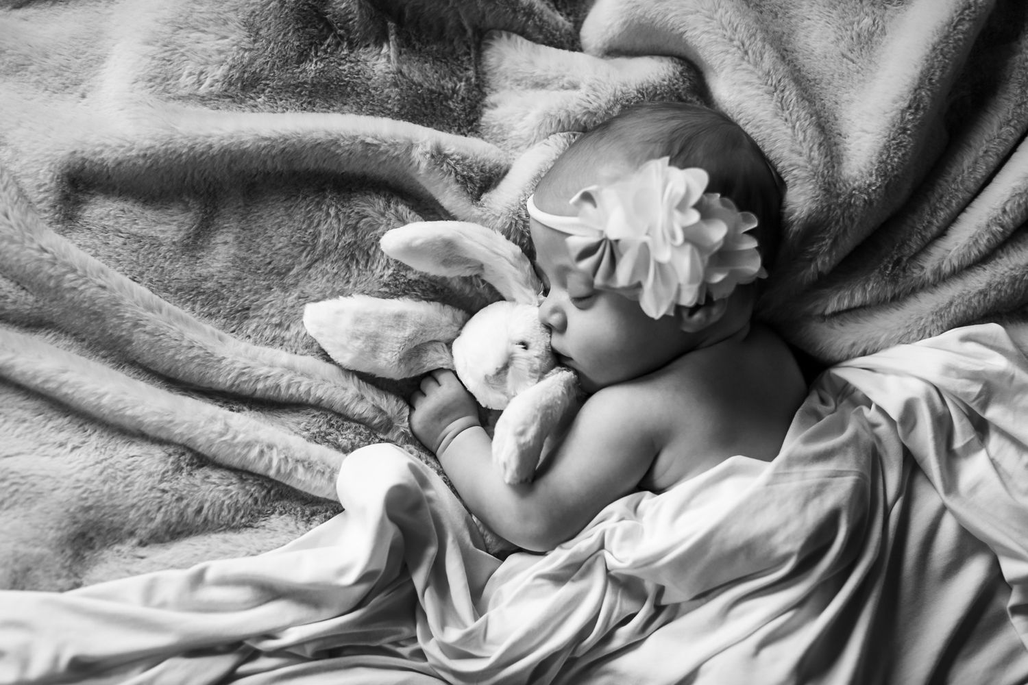 Black and white image of peacefully sleeping baby wrapped in soft blankets.