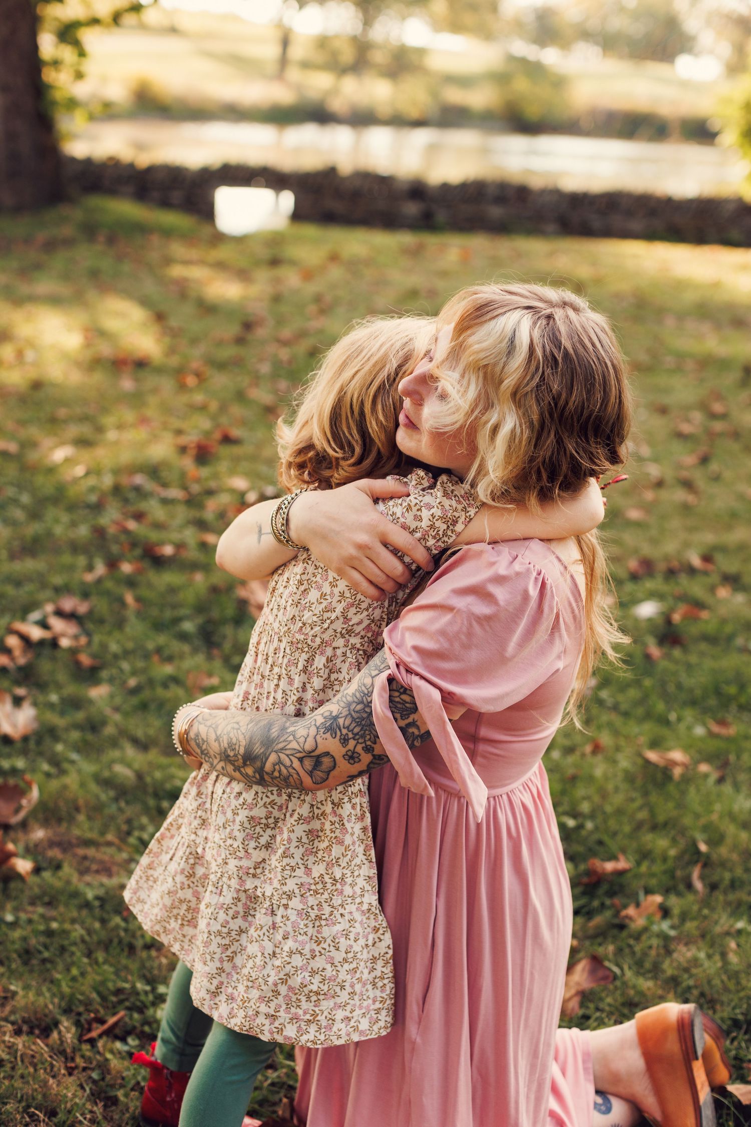 Children share a sweet embrace while wearing pink and floral dresses on a sunny autumn day.