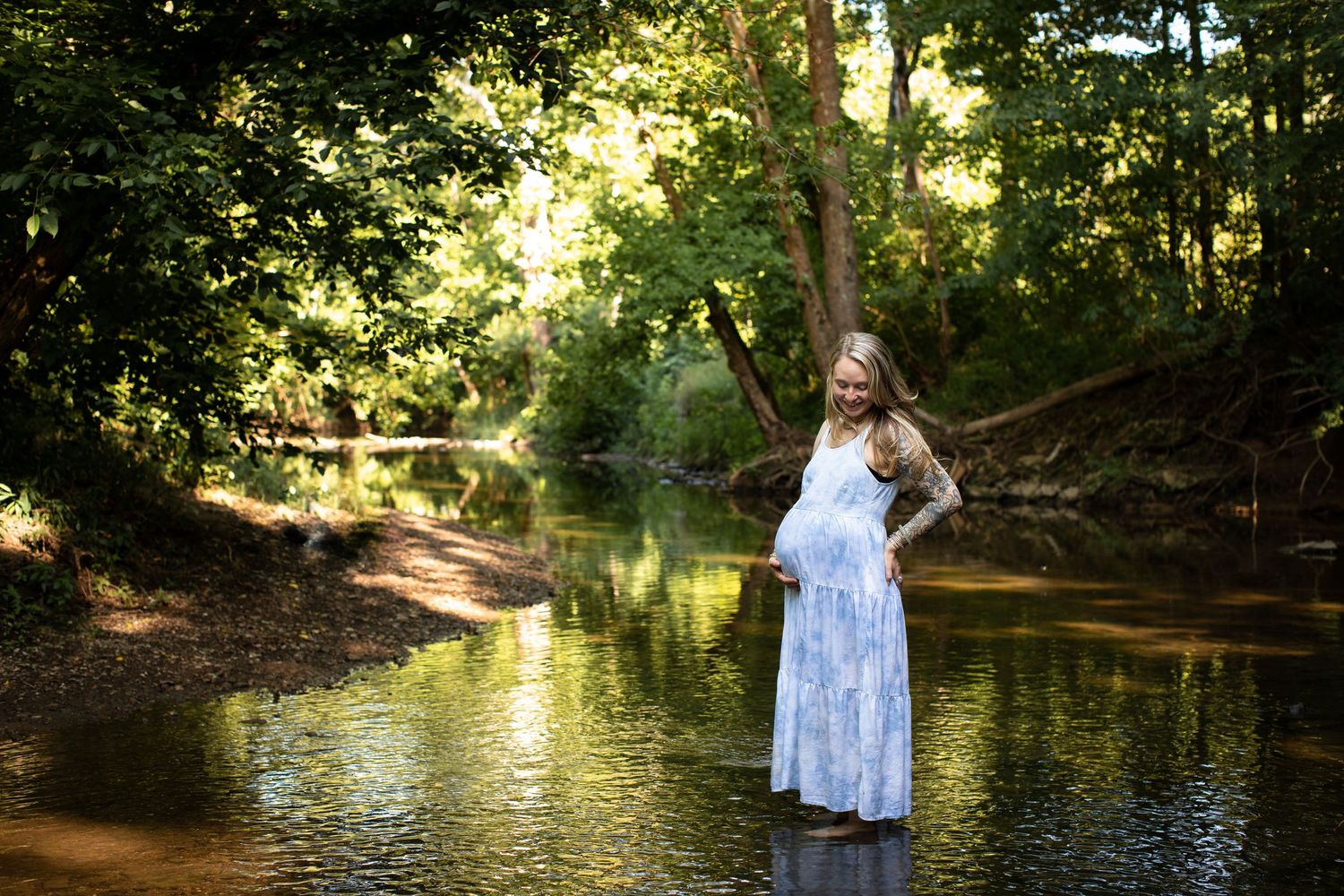 Scenic creek in a wooded area with golden sunlight filtering through trees creating a peaceful natural setting.