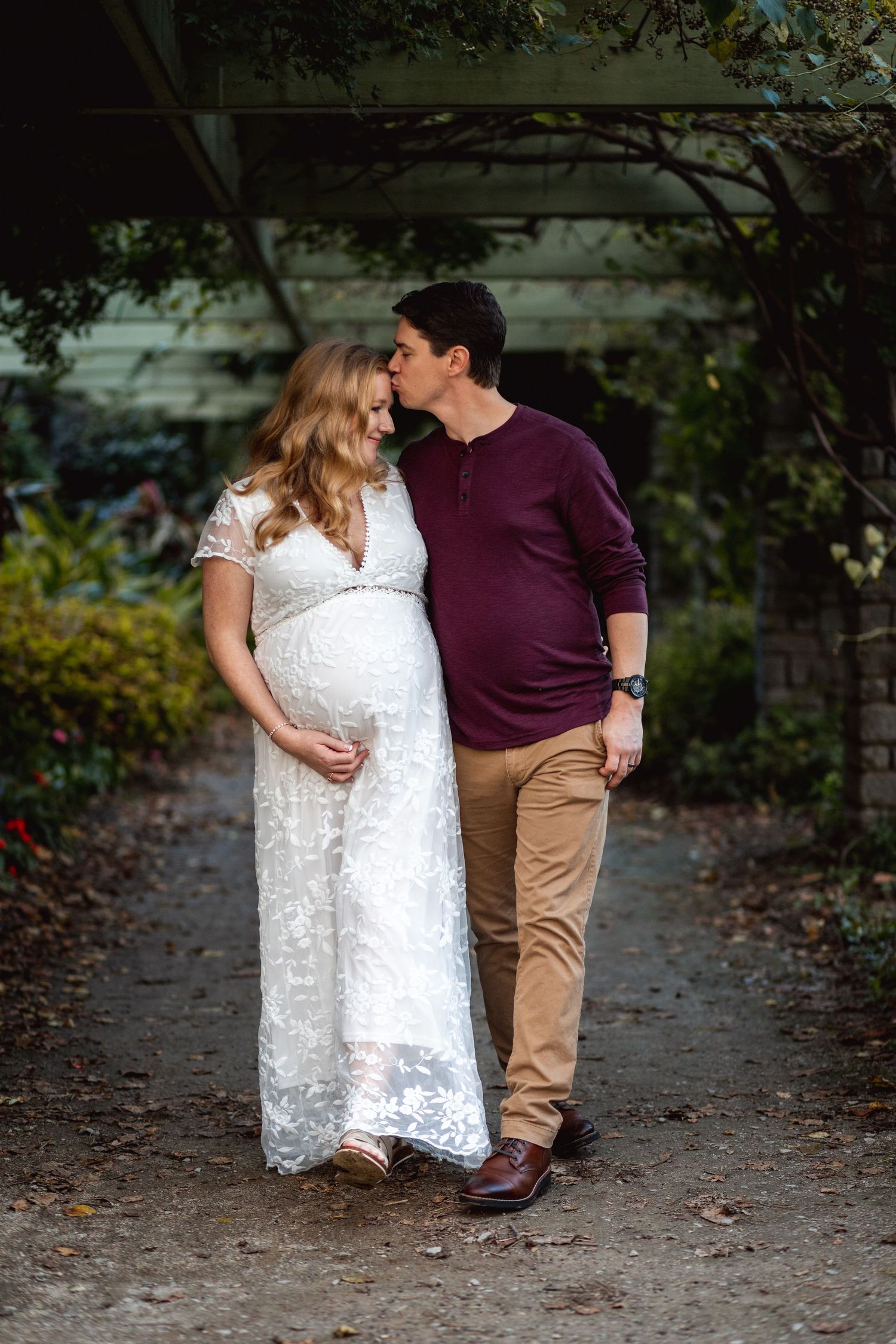 A romantic maternity photo of a couple on a garden path under an archway.