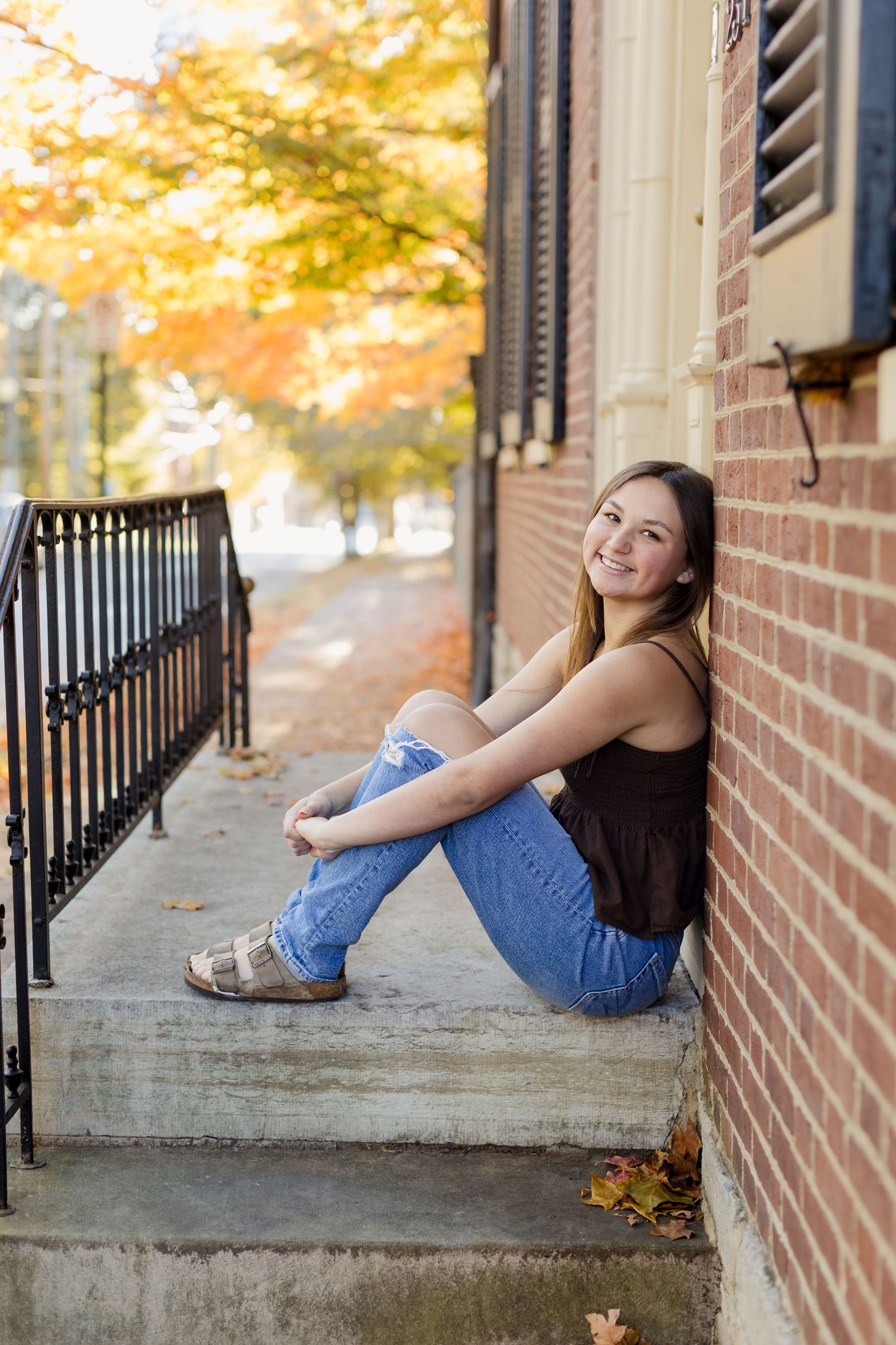 Casual portrait on brick steps during autumn with fall foliage in background.