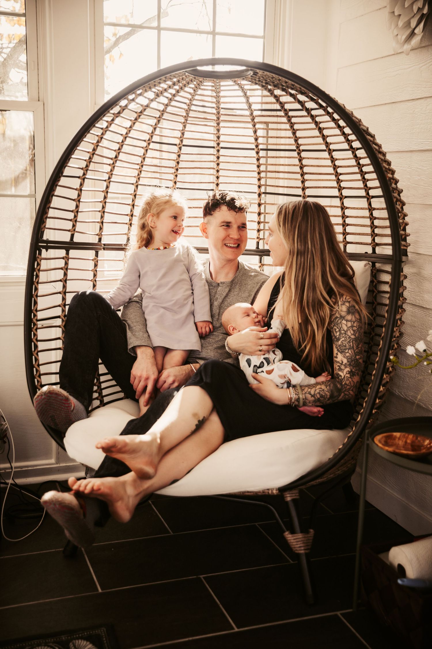 Family relaxing together in large woven egg chair indoors.
