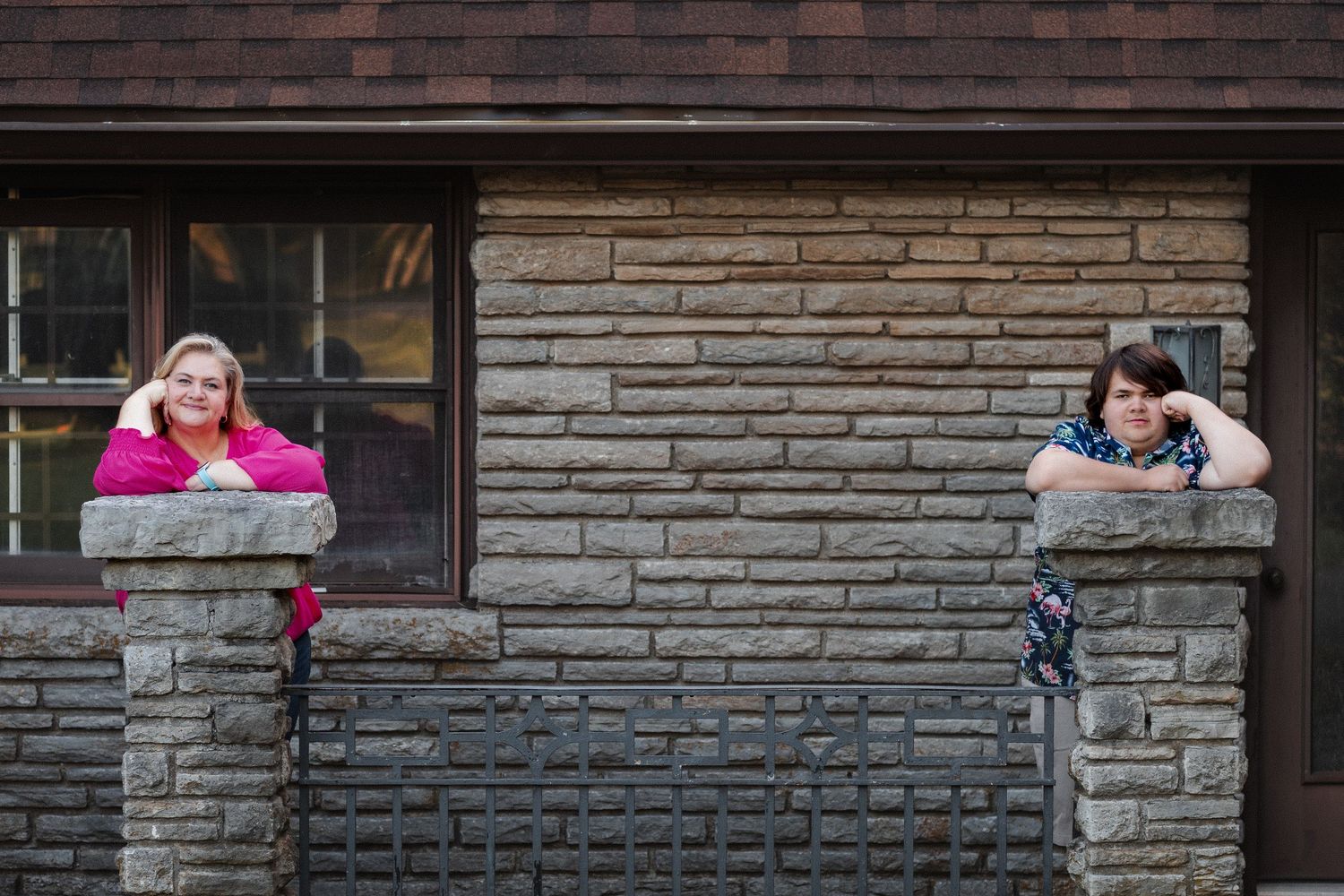 A person sits on a ledge against a brick wall while looking at their phone in an urban setting.