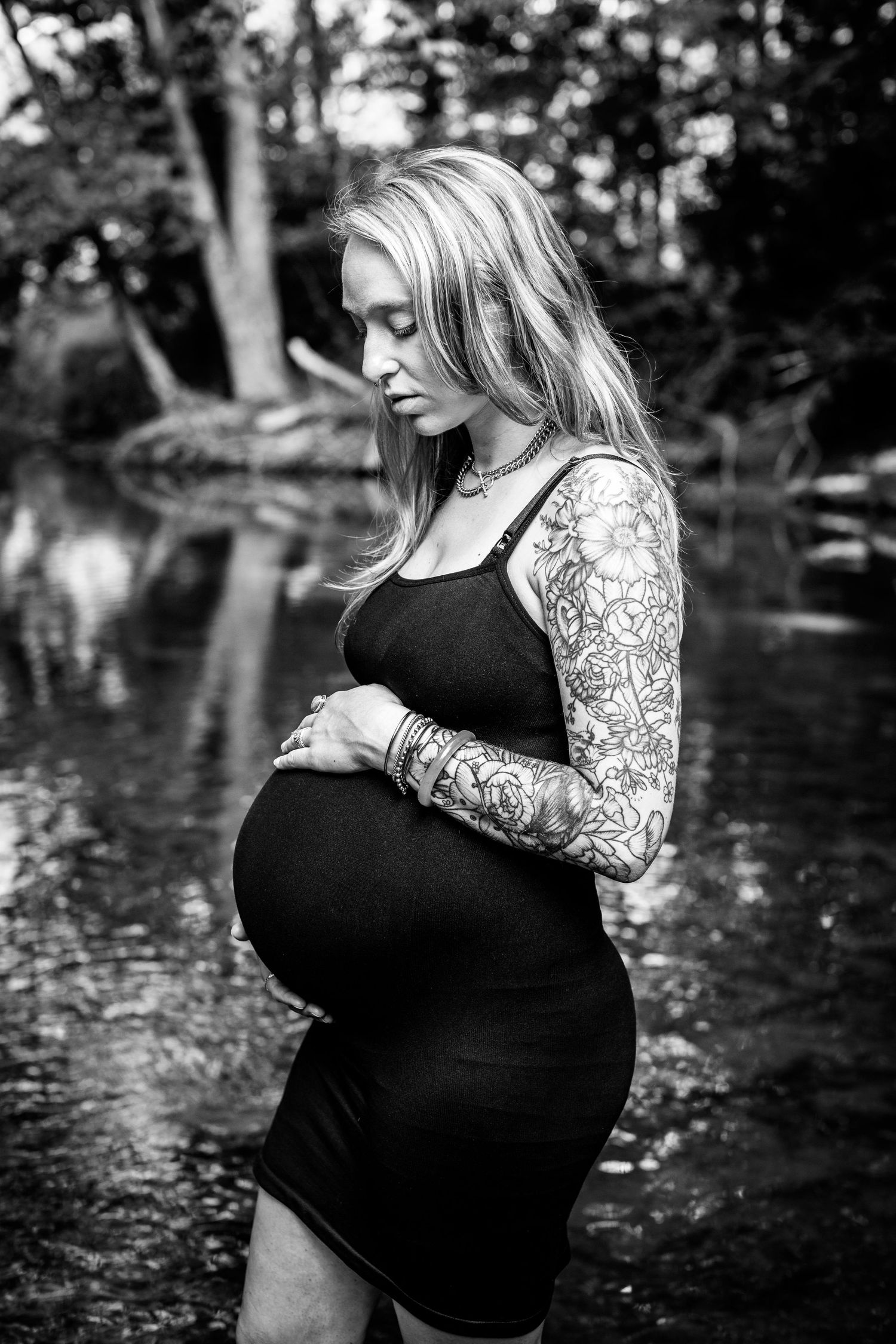 Black and white maternity portrait showing artistic tattoo details in natural setting.