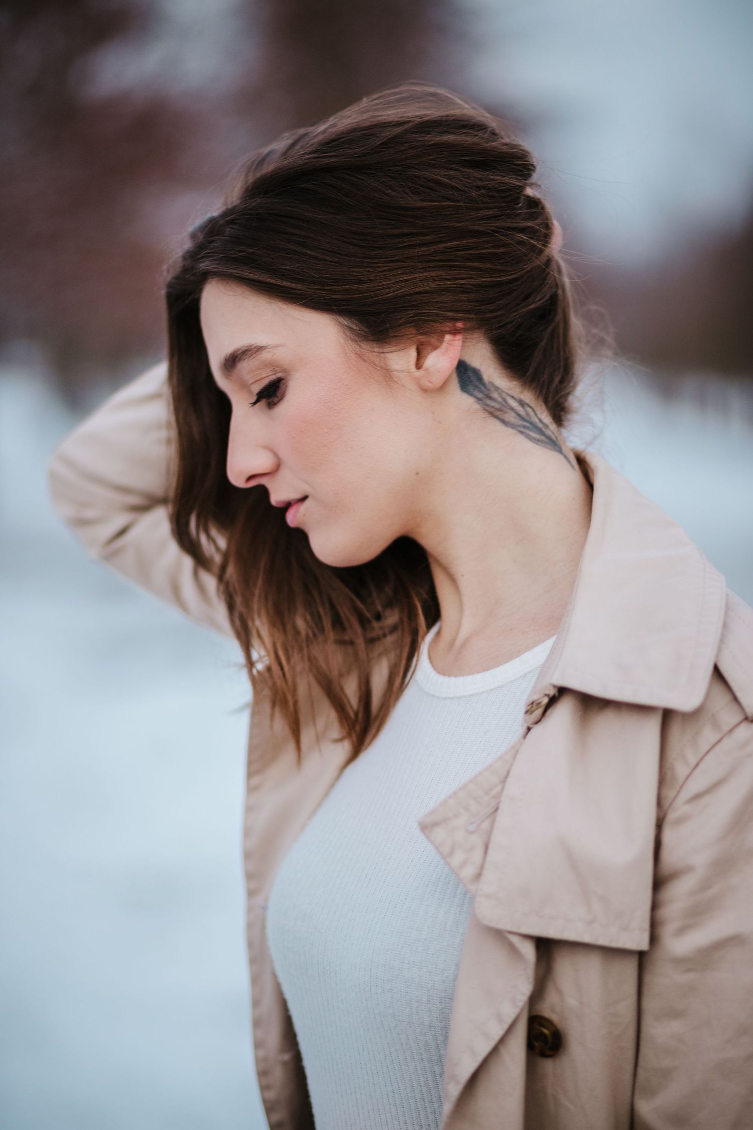Side profile portrait outdoors wearing a beige trench coat against a snowy winter background.