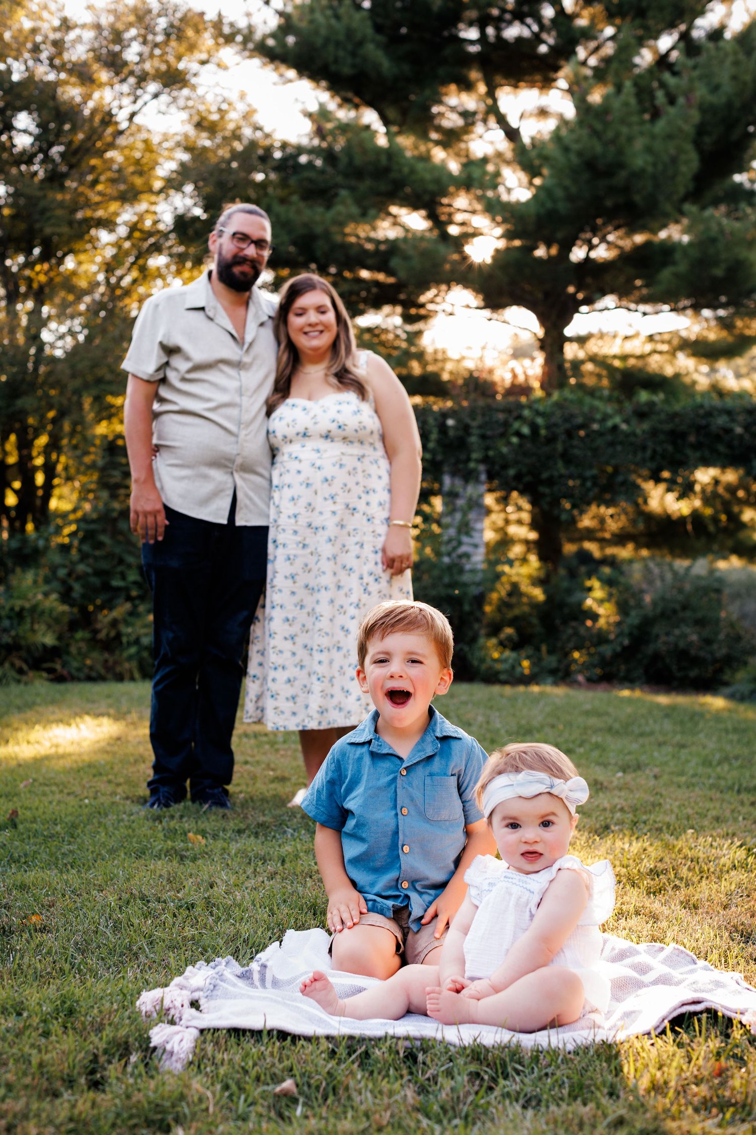 Family portrait session in a grassy field at sunset with warm golden lighting.