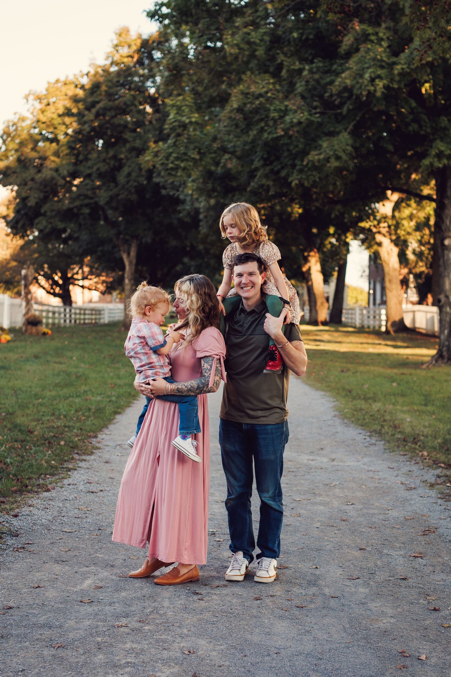 A family in coordinated pink and navy outfits walks together on a tree-lined path during golden hour.