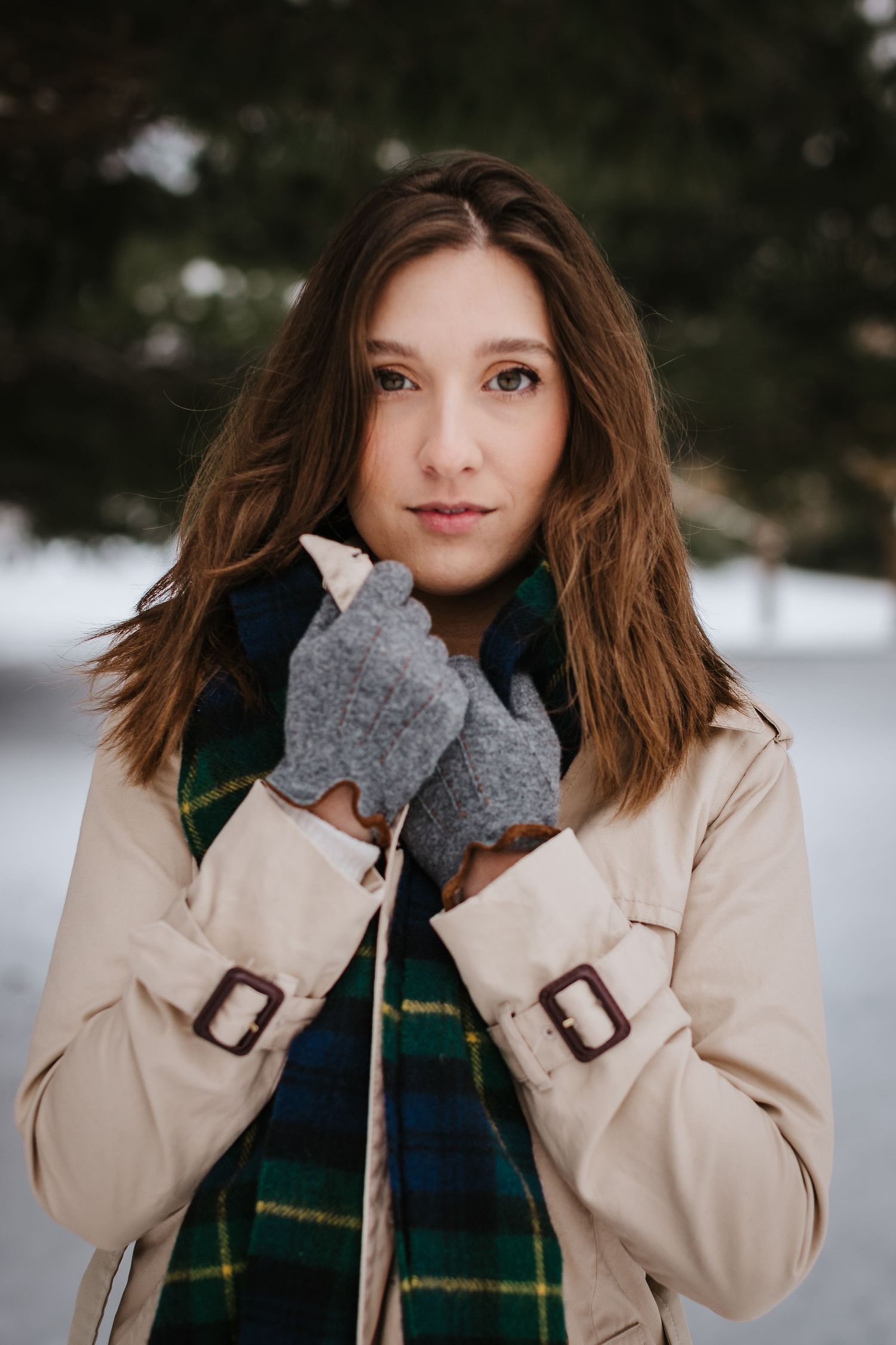 Winter portrait featuring a beige coat, plaid scarf and grey gloves in a snowy setting.