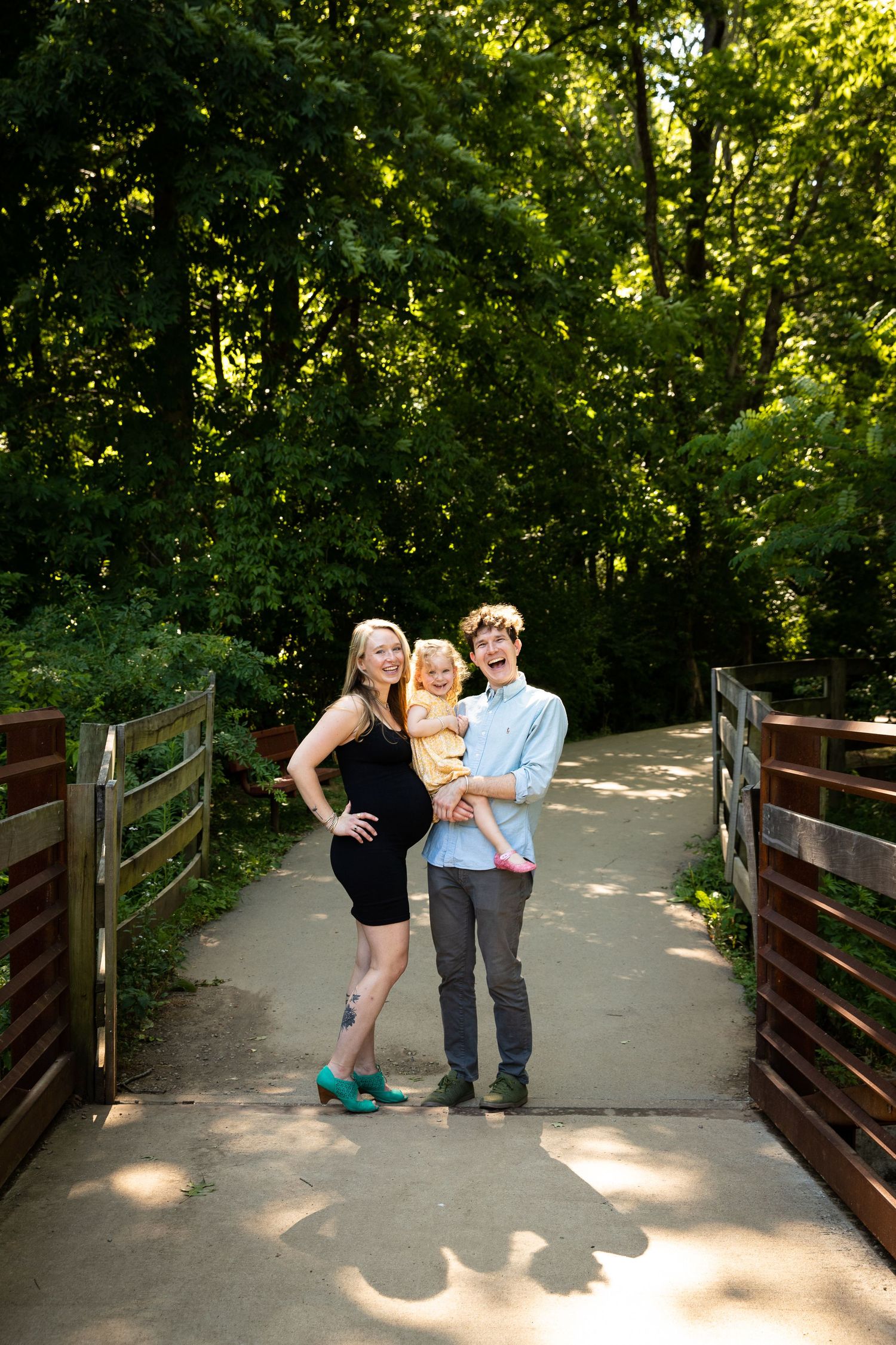 Family standing on wooden bridge path surrounded by lush green forest.