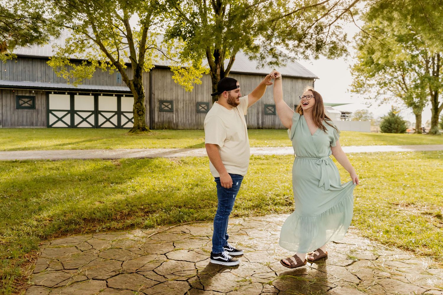 Dancing couple enjoying a playful moment on a stone patio near a barn.