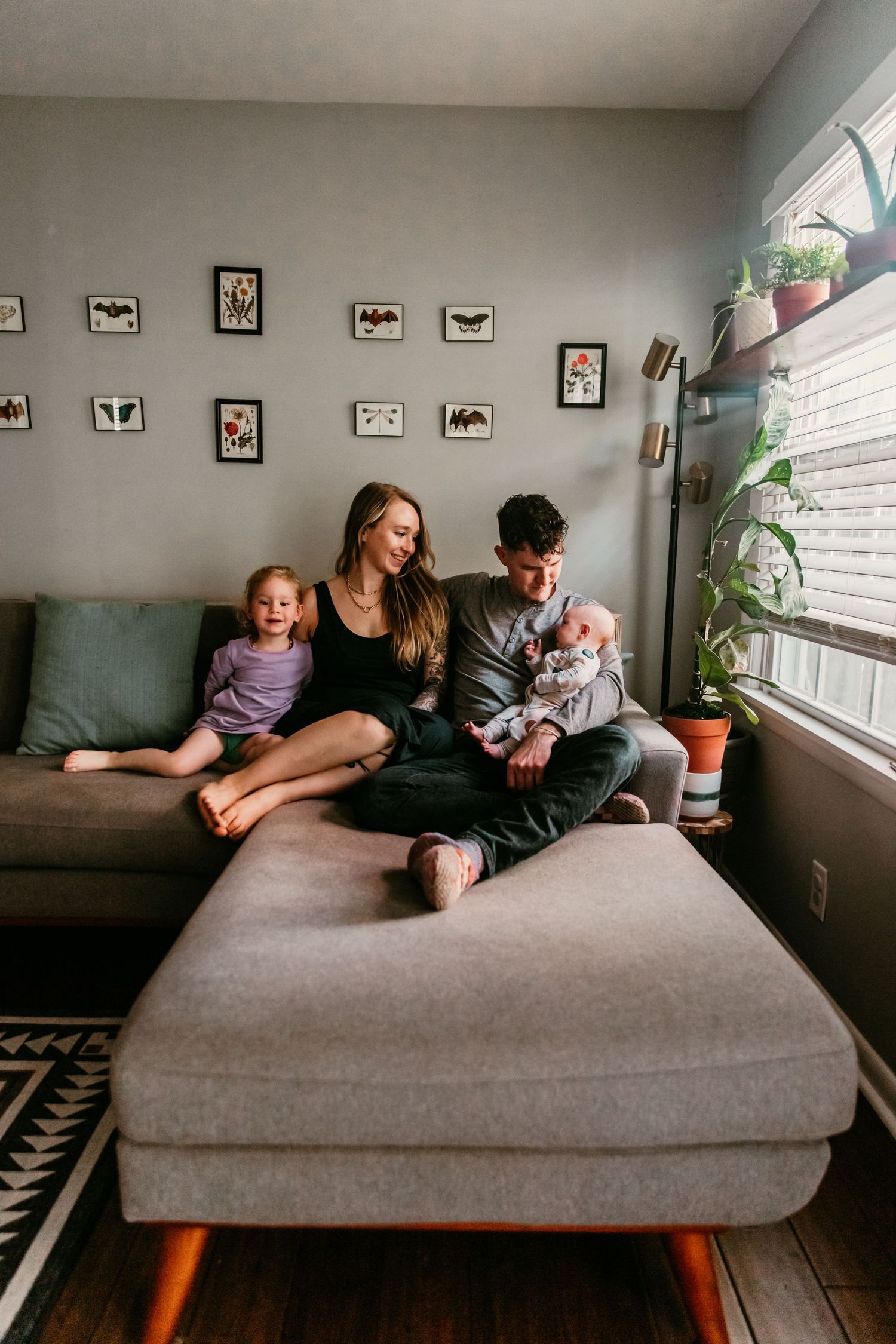 Family relaxing together on a gray sectional sofa in a cozy living room with framed art on the walls.