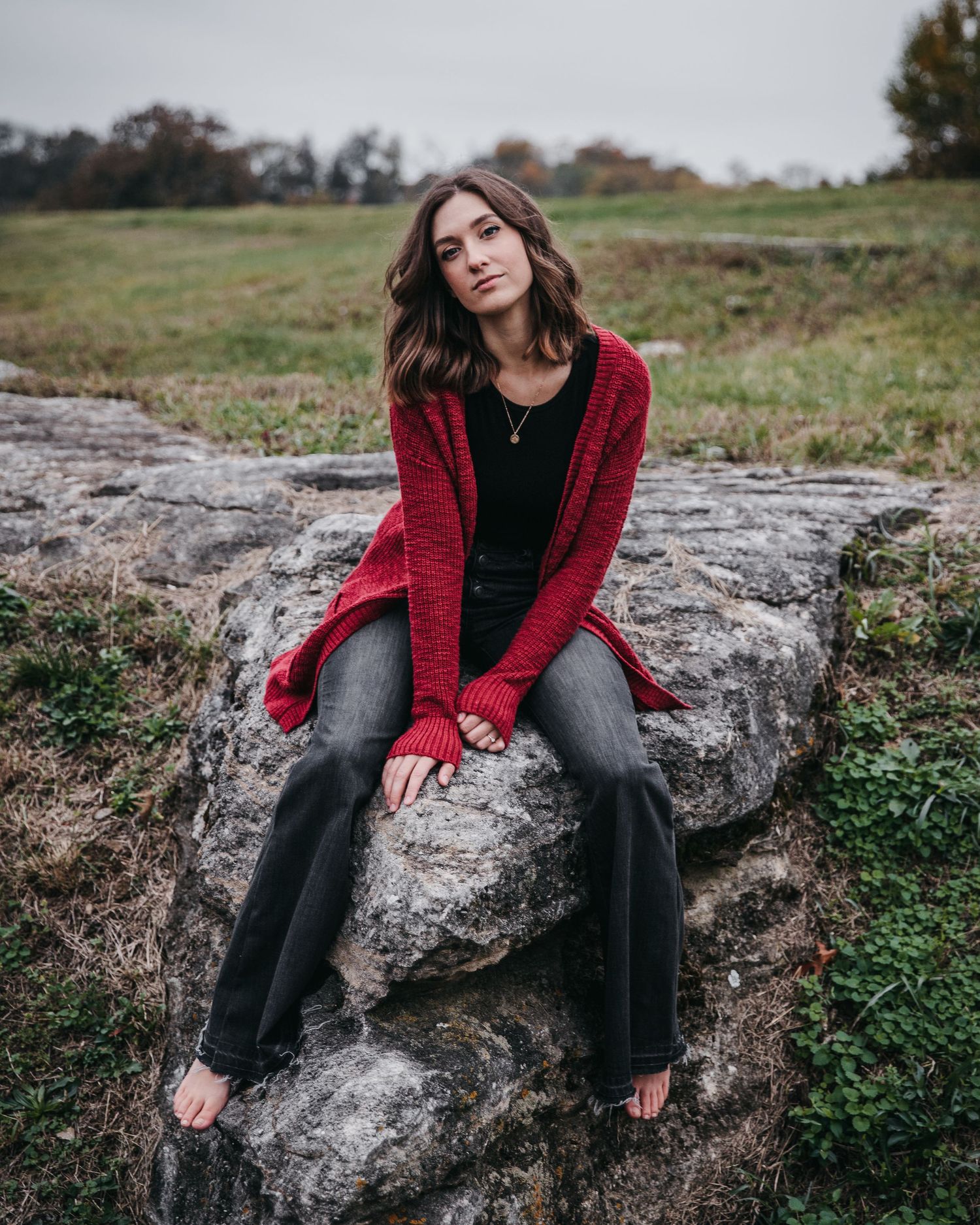 Portrait on rocky outcrop wearing red cardigan and black jeans.