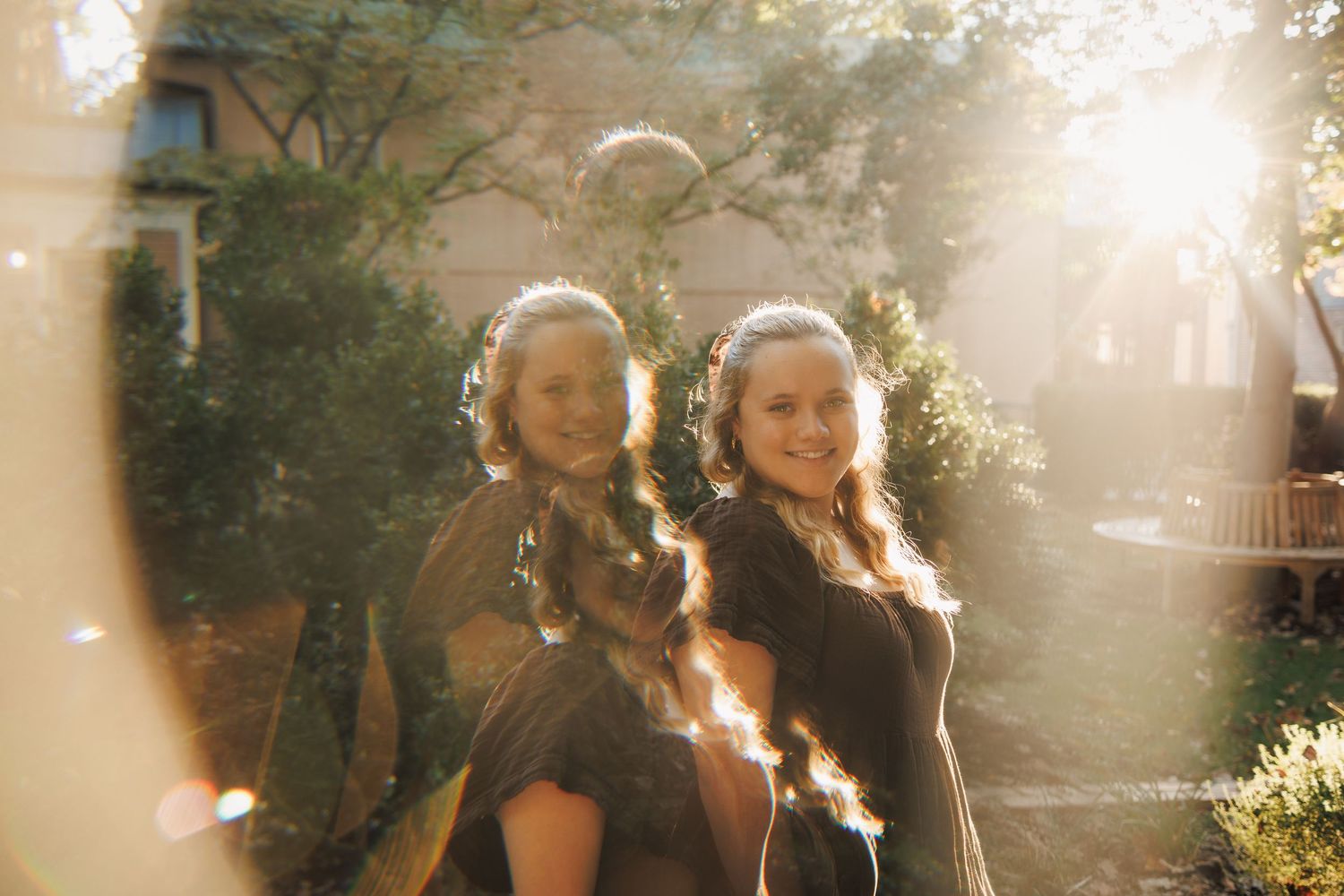 Two people pose together outdoors in warm sunlight with a lens flare effect creating a dreamy vintage atmosphere.