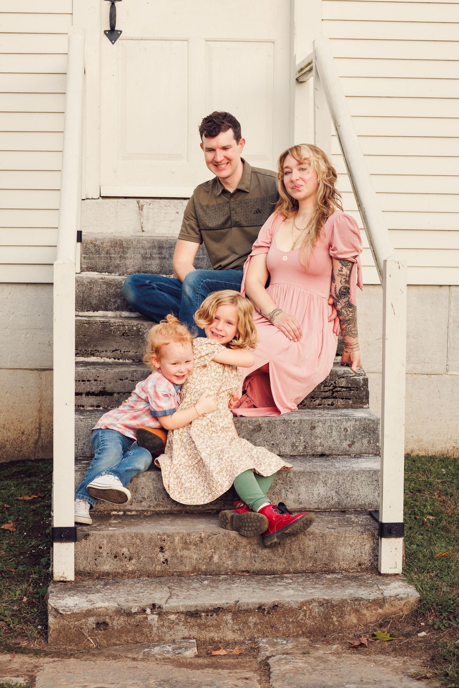 Family sits together on white porch steps during an outdoor photo session at sunset.