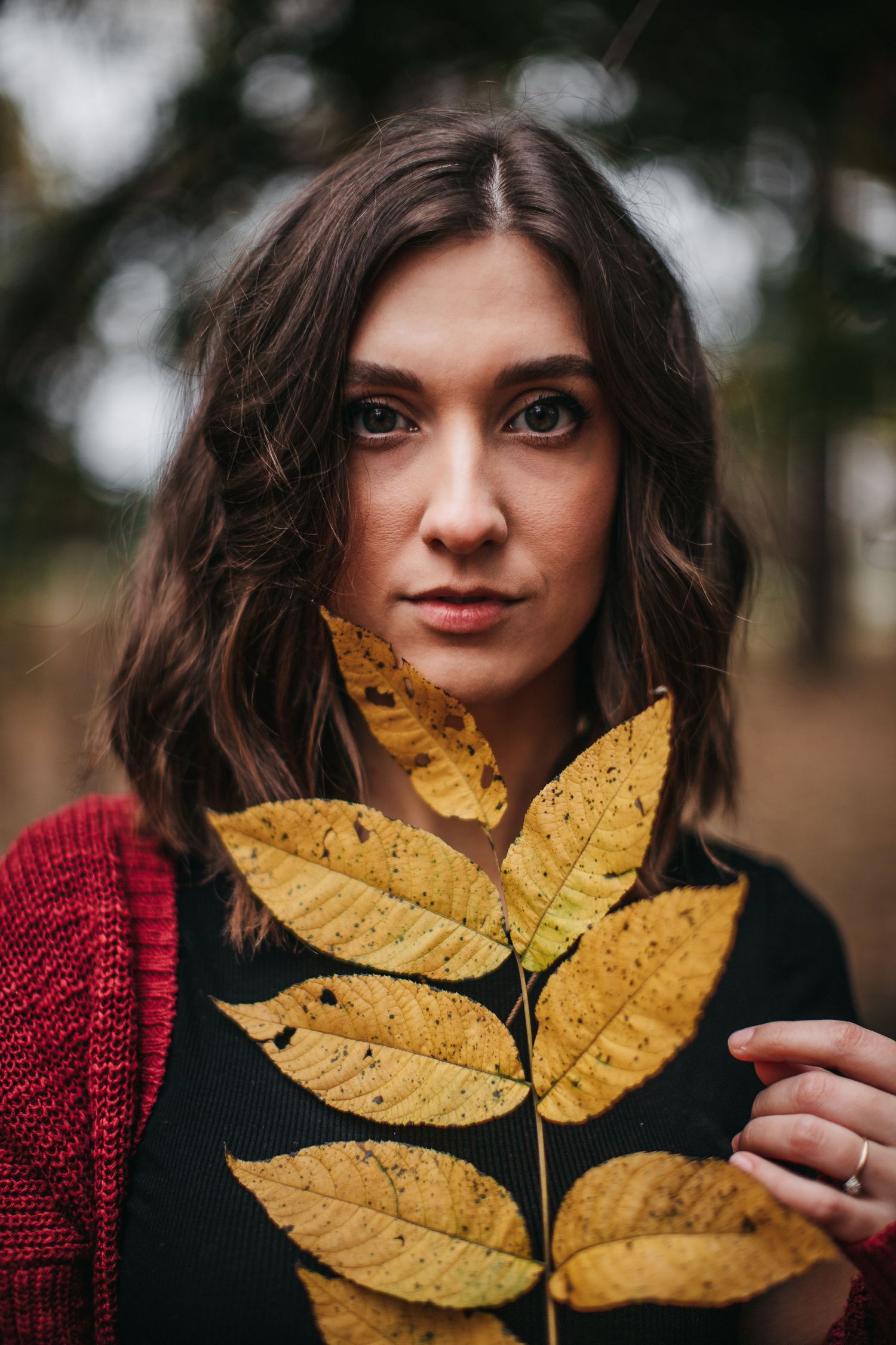 Portrait with autumn yellow leaves and red sweater in moody outdoor setting.