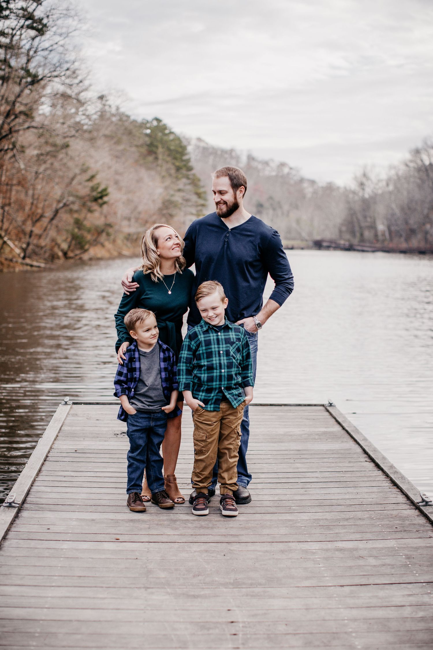 A family poses together on a wooden dock overlooking a serene lake.